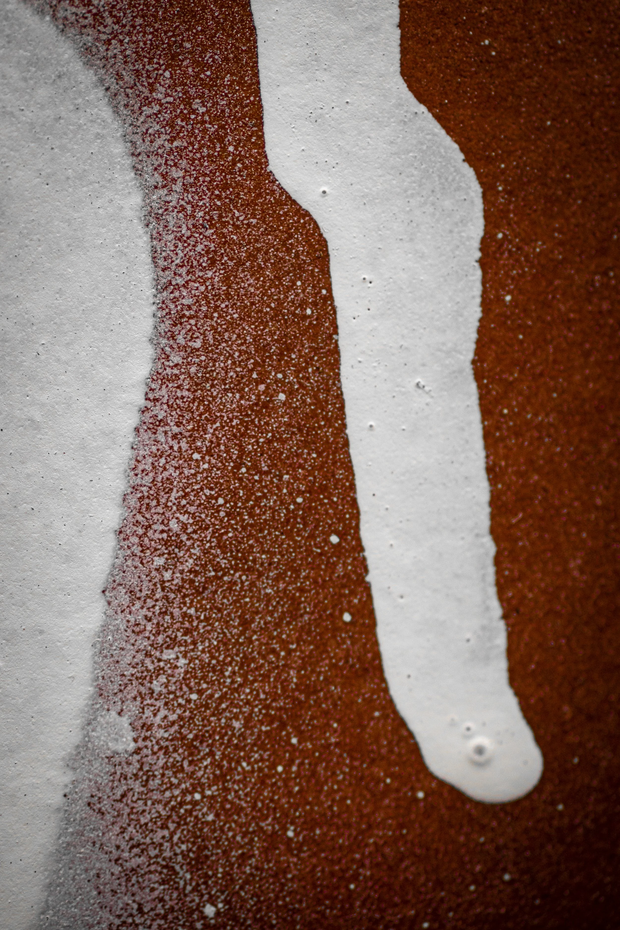 Abstract macro photograph of white paint sprayed over an orange brick wall creating painterly contrast of white on brown.