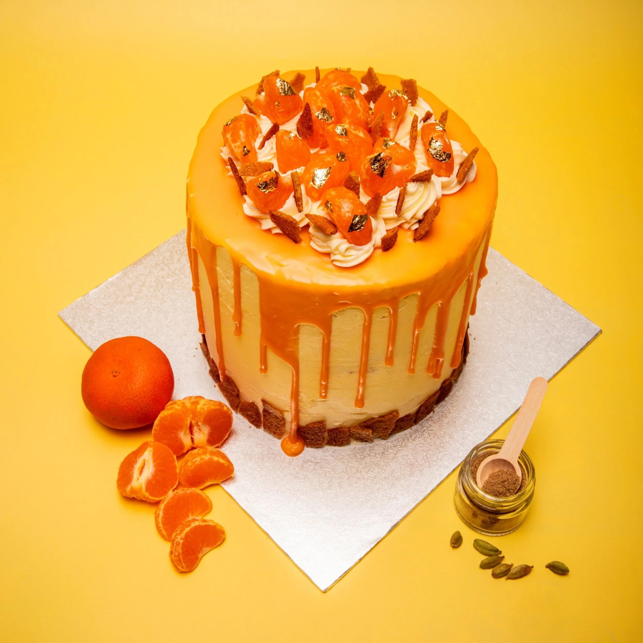 Commercial food photography of elegant caramel drip cake with gold leaf, mandarin oranges and cardamom styled on yellow background
