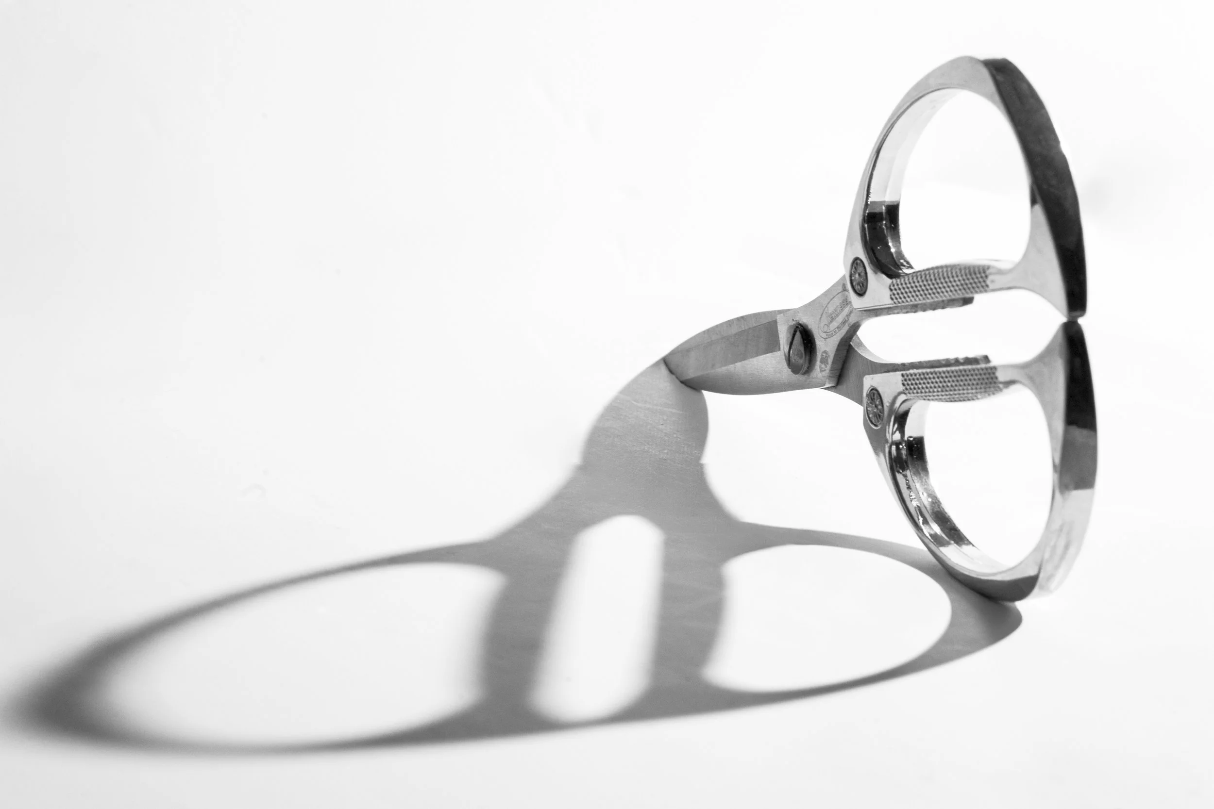 Artistic black and white still life of decorative scissors with crystal details casting bold shadow on white surface.