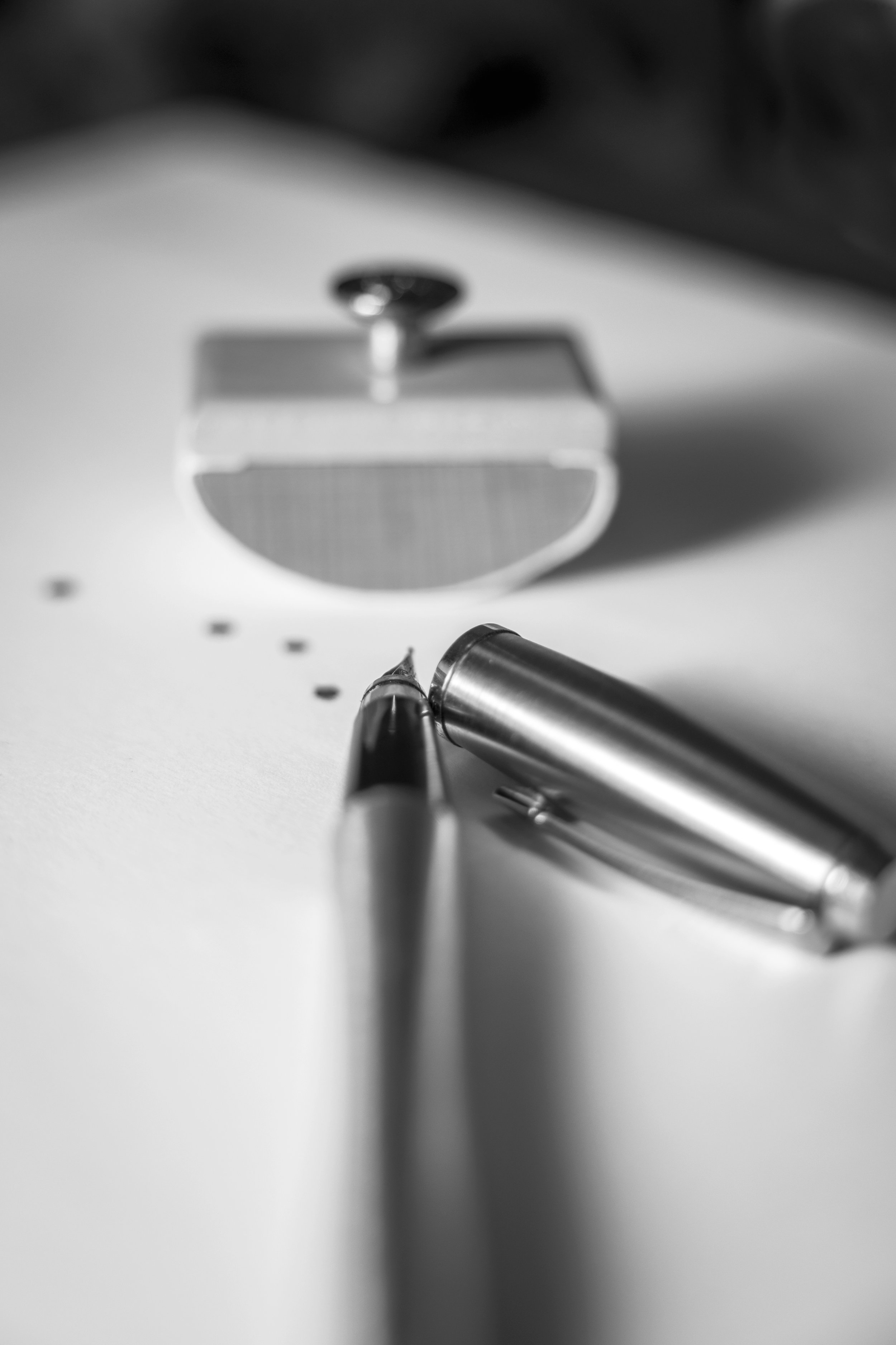 Still life photography, black and white close-up of fountain on white paper with blurred bloating paper in the background.
