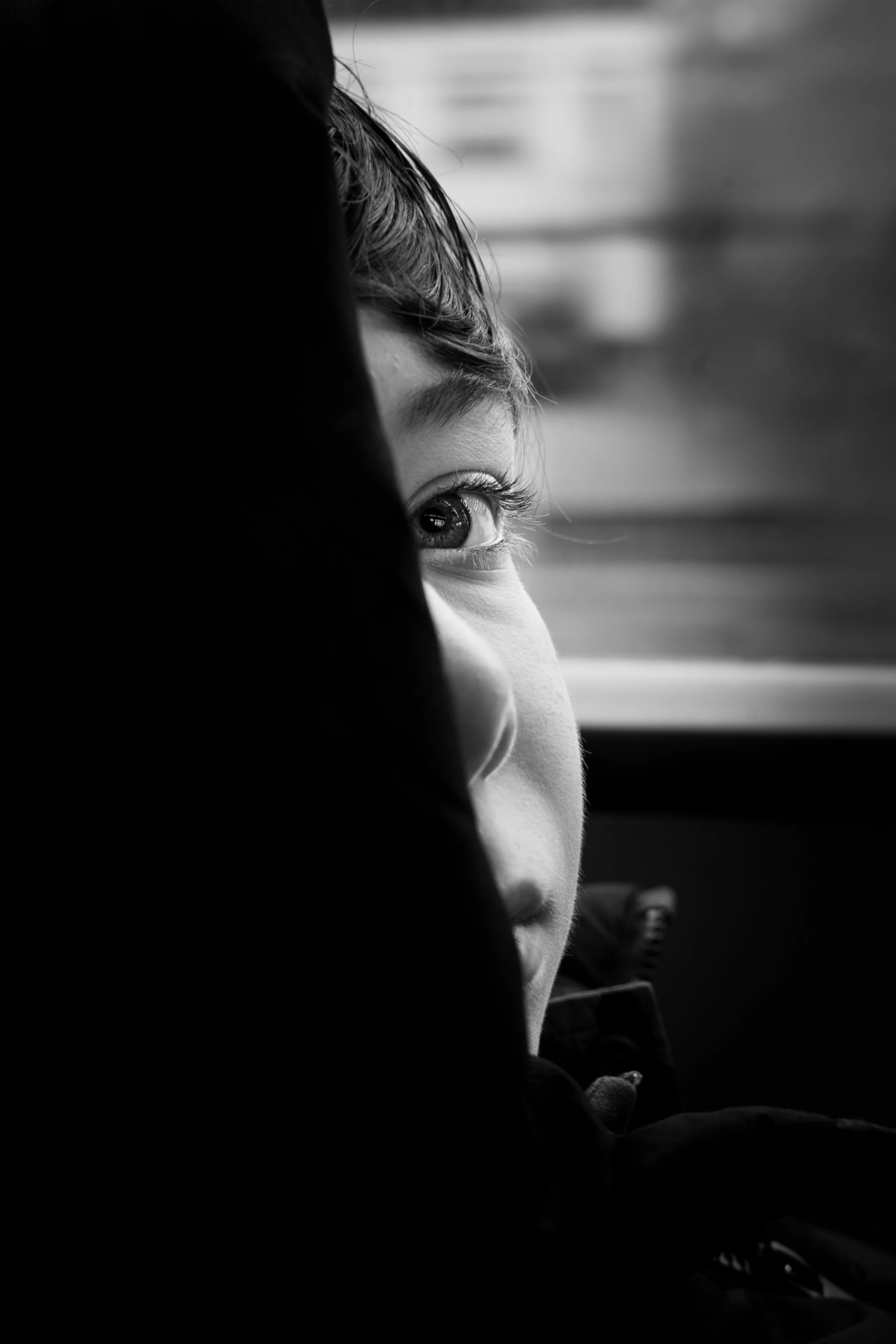 Black and white fine art street photography of young child's eye and profile emerging from deep shadow on public transport.