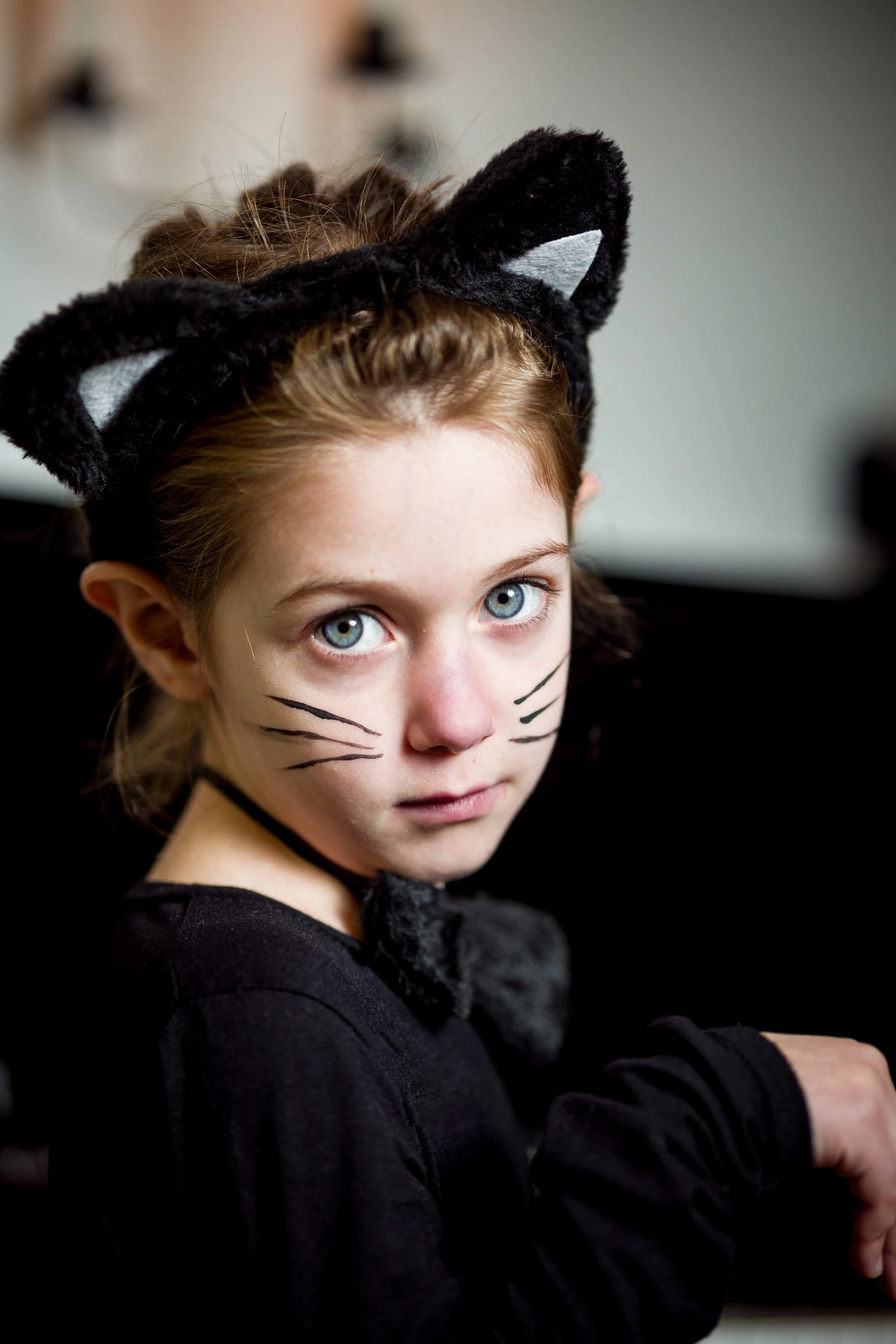 Studio lighting children's portrait photography of girl in black cat costume with face paint whiskers and cat ear headband.