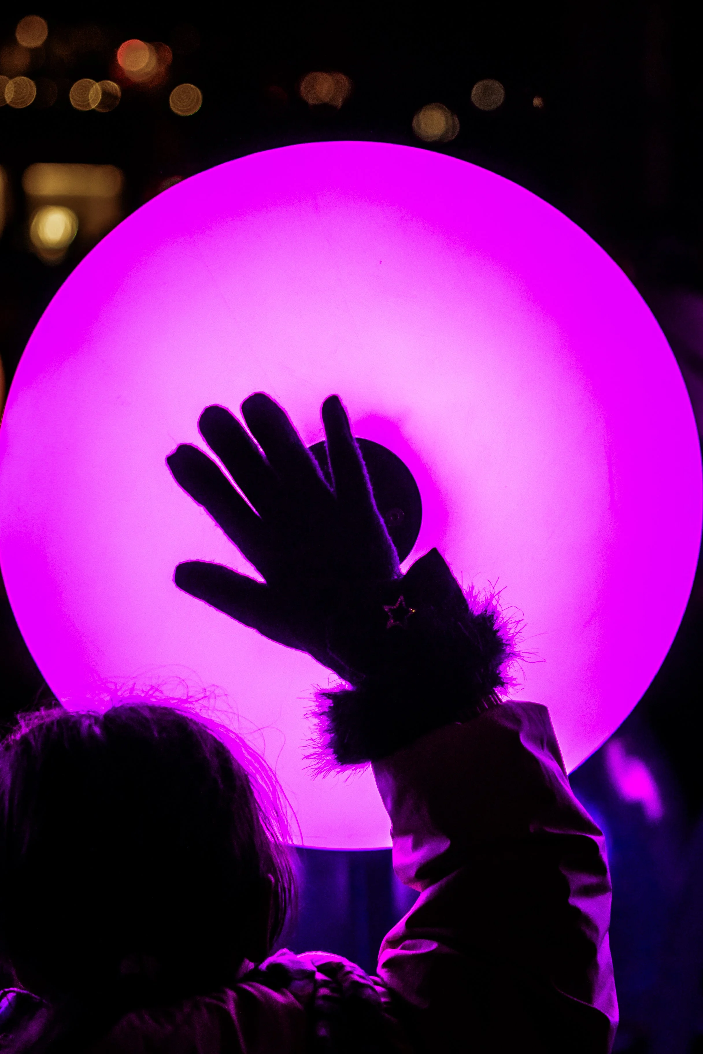 Dramatic night photography of child's silhouette with raised gloved hand against vibrant purple circular light installation.