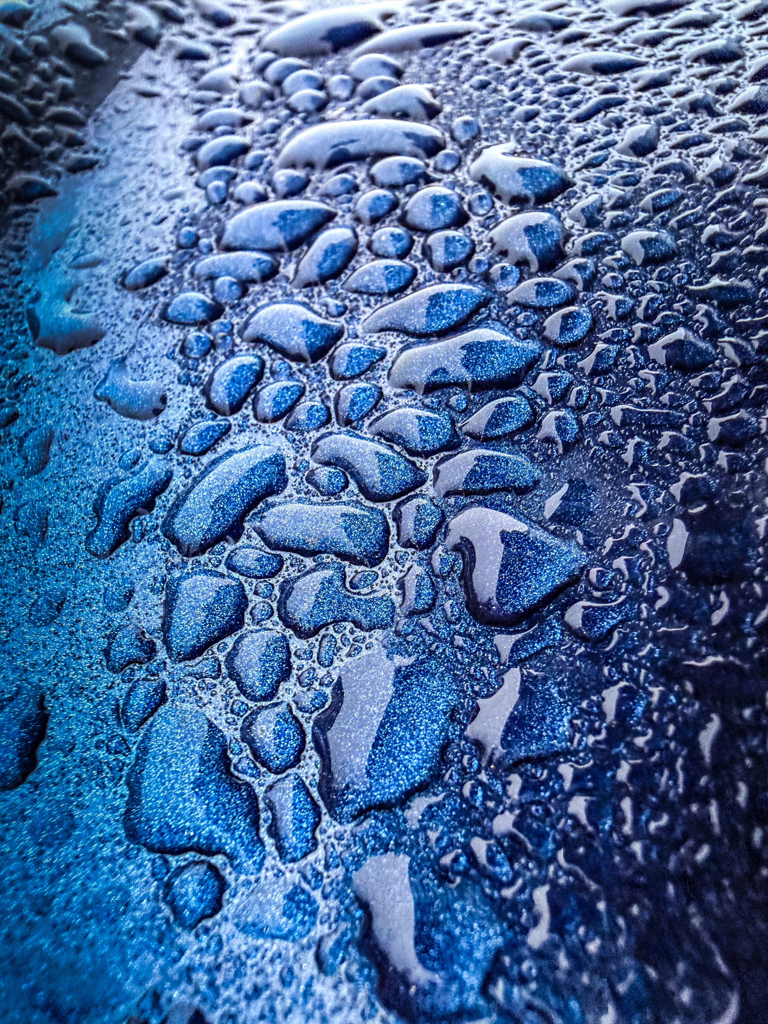 Macro photography of water droplets on blue metallic surface creating abstract texture and pattern.