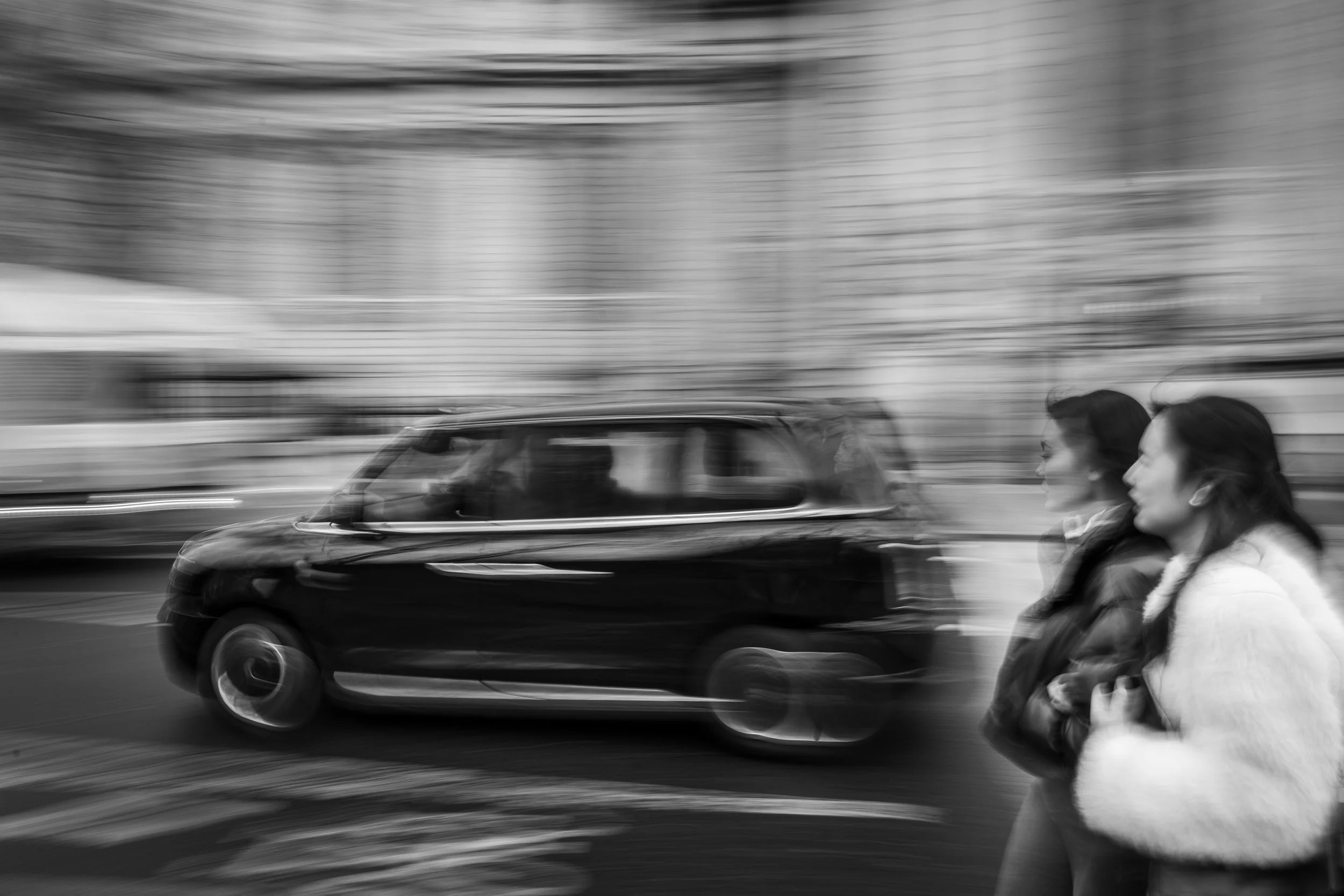 Black and white experimental urban street photography with motion blur panning technique of car and pedestrians in London city street.