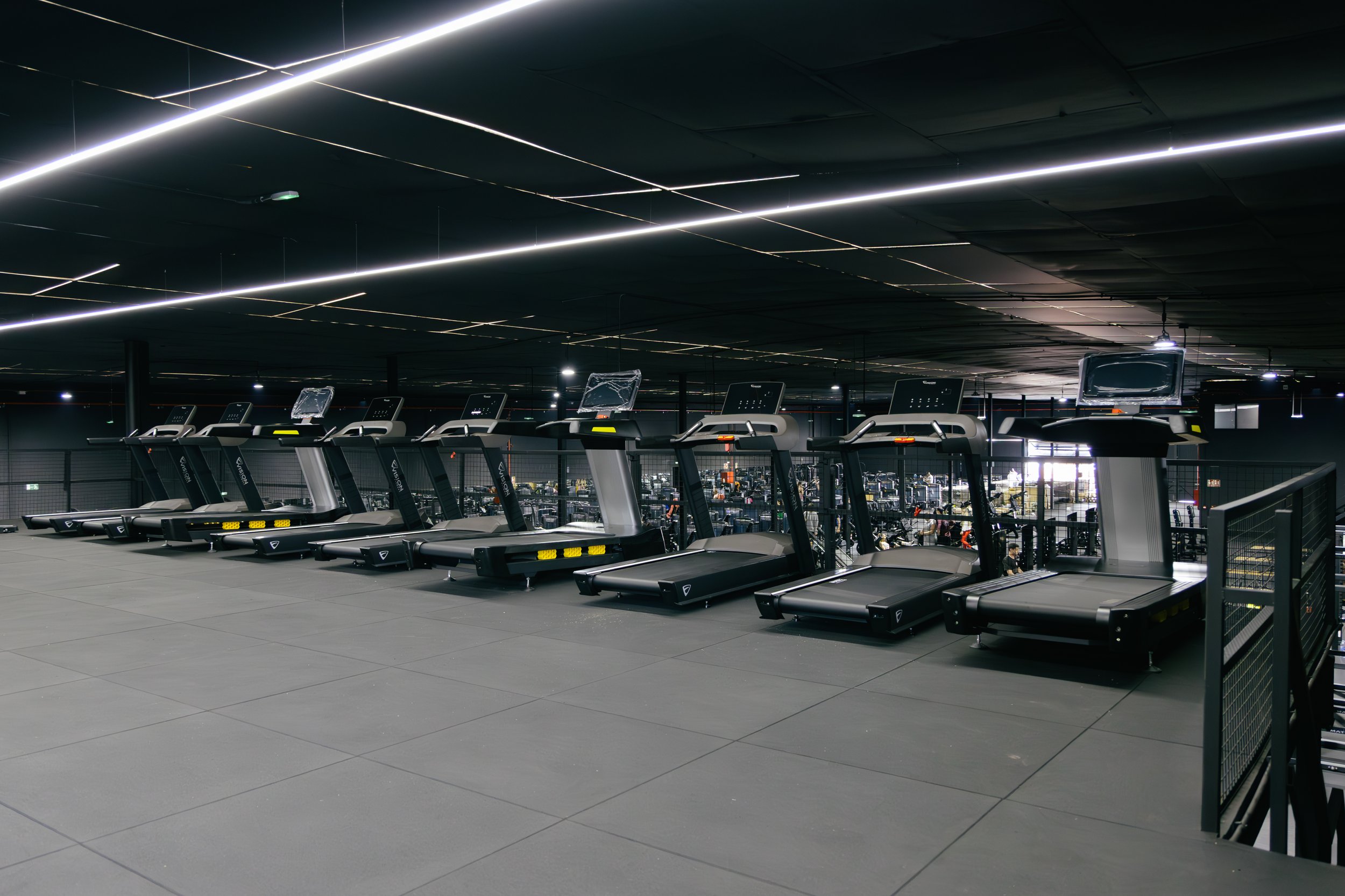 Gimnasio moderno con varias caminadoras en fila, techo oscuro y iluminación minimalista.