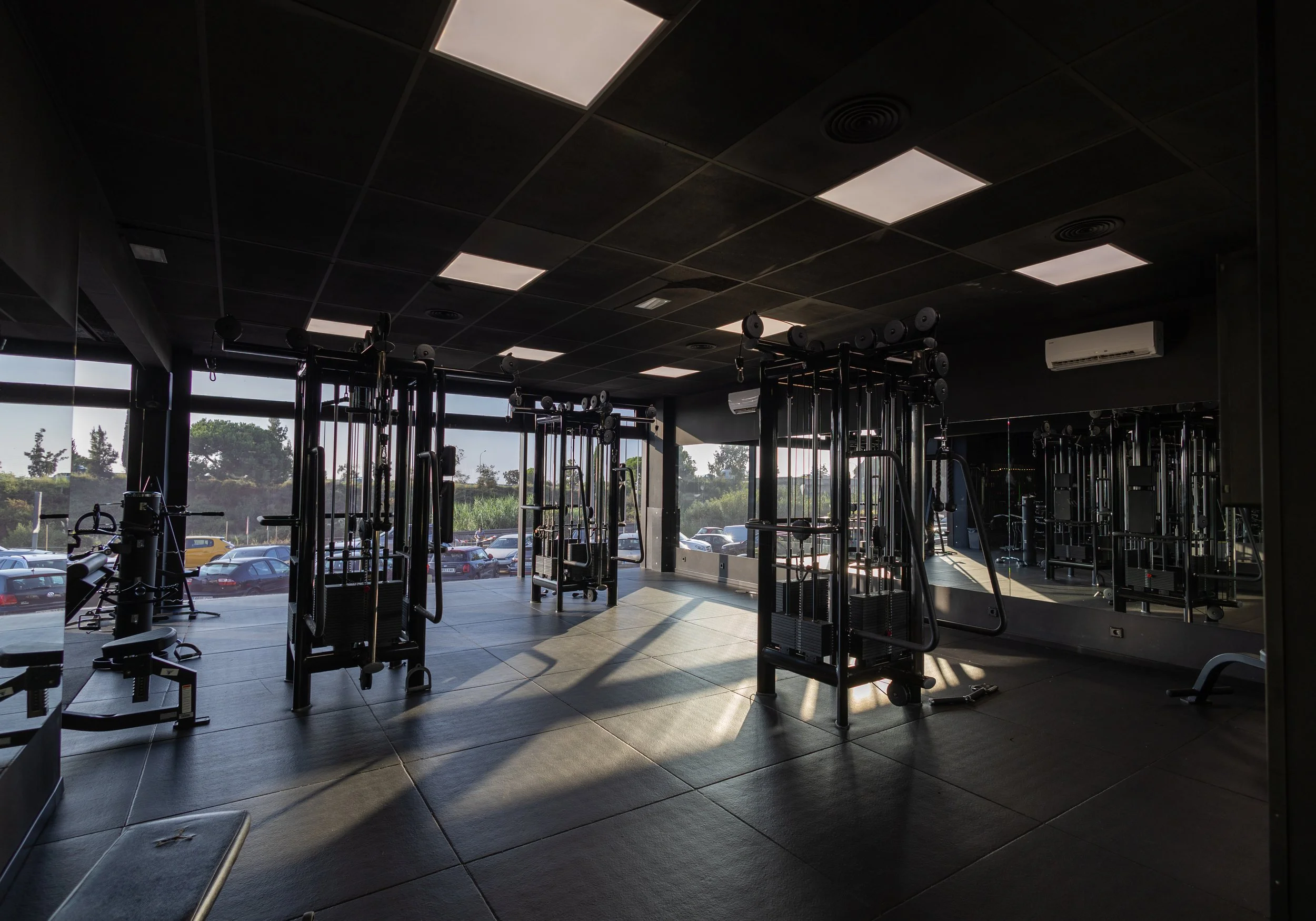 Gimnasio con equipos de entrenamiento y ventanas que dejan entrar luz natural