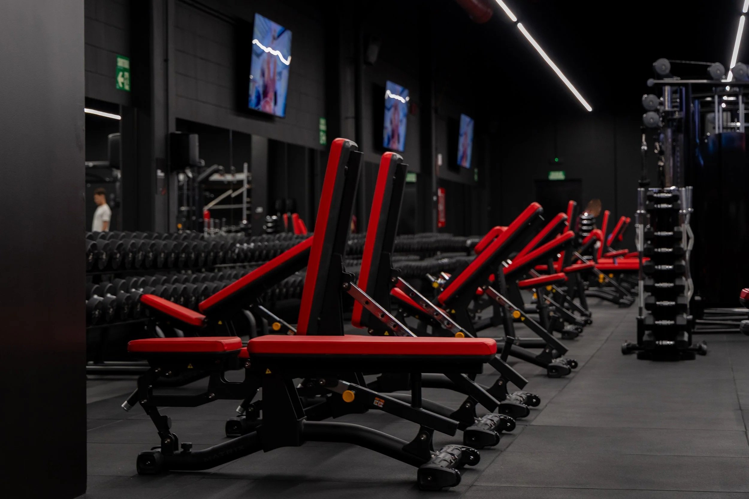 sala de gimnasio vacía con sillas de entrenamiento y pesas en un ambiente oscuro con pantallas en la pared