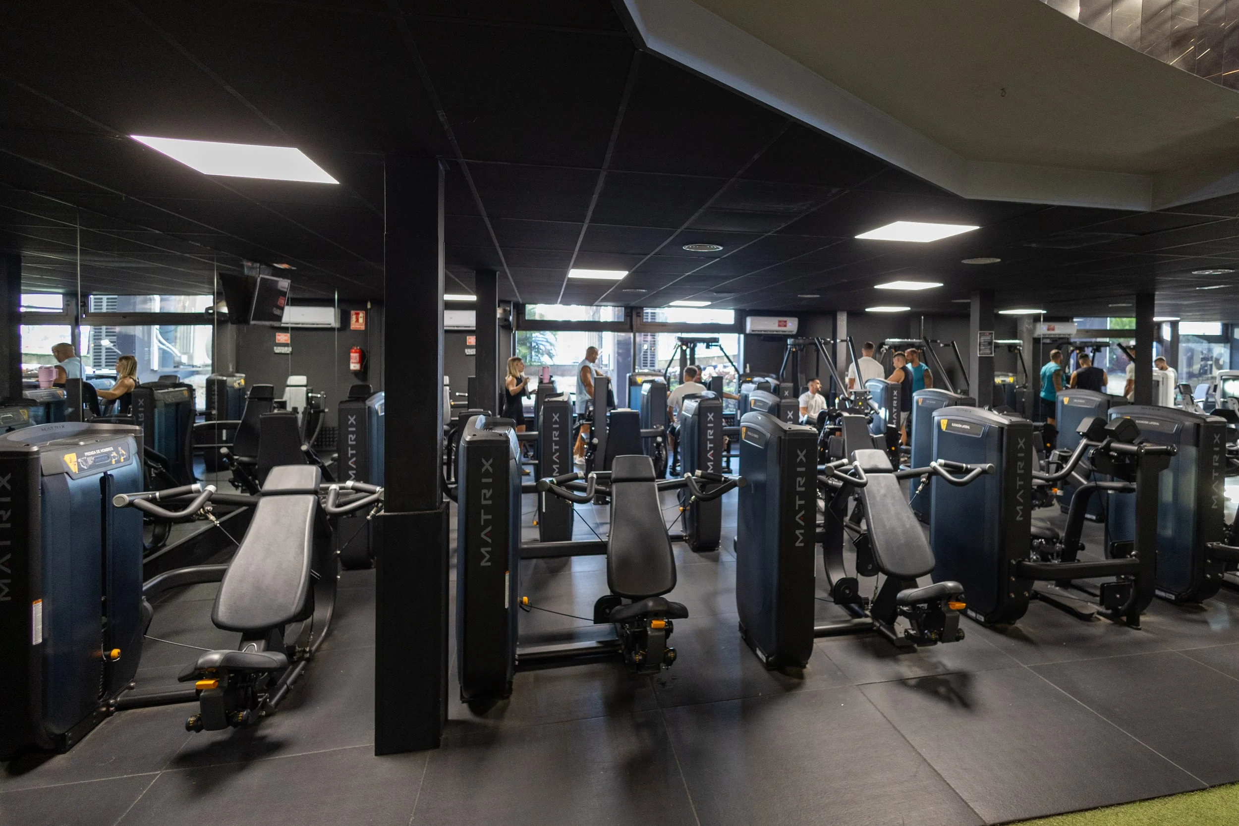 Sala de gimnasio con máquinas de ejercicio y varias personas entrenando.