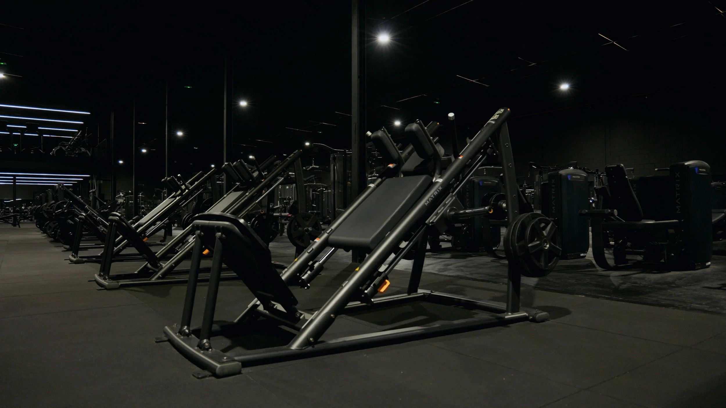Gimnasio con equipo de entrenamiento moderno en un ambiente oscuro con iluminación tenue.