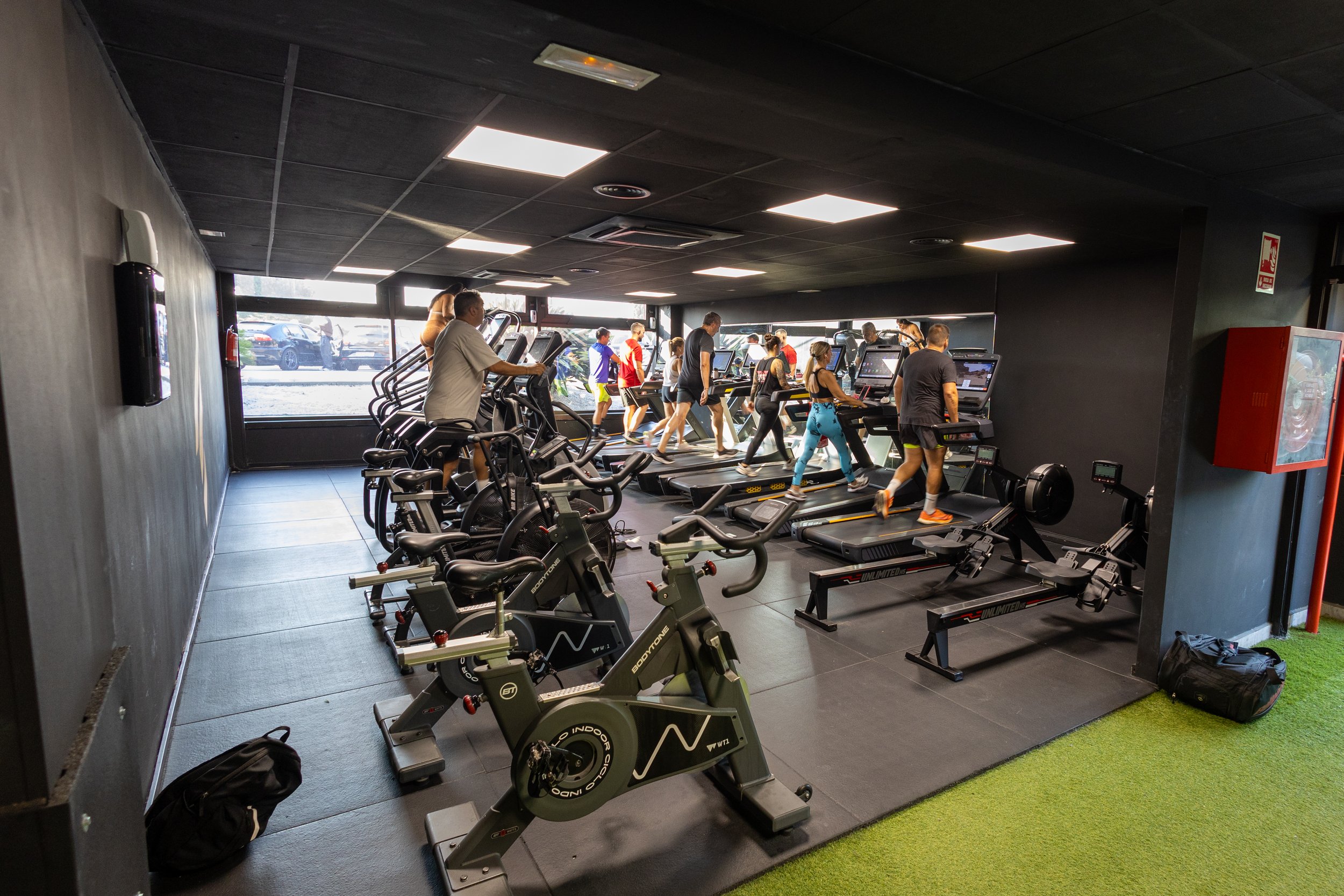 Gente haciendo ejercicio en una sala de gimnasio con máquinas de cardio y pesas.