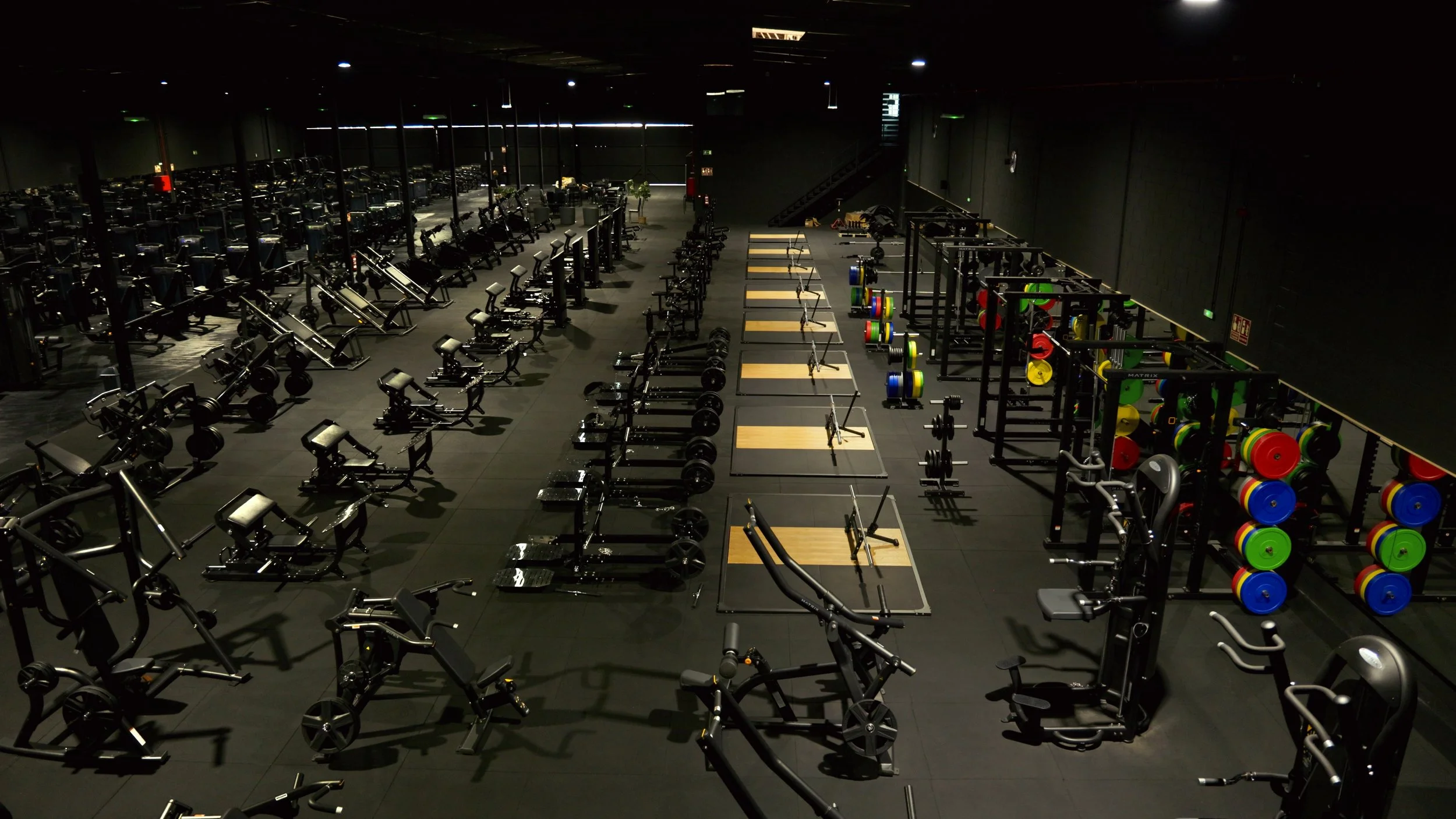 Interior de un gimnasio con varias máquinas de ejercicio, pesas y área de pesas libres, en un espacio amplio y bien iluminado.