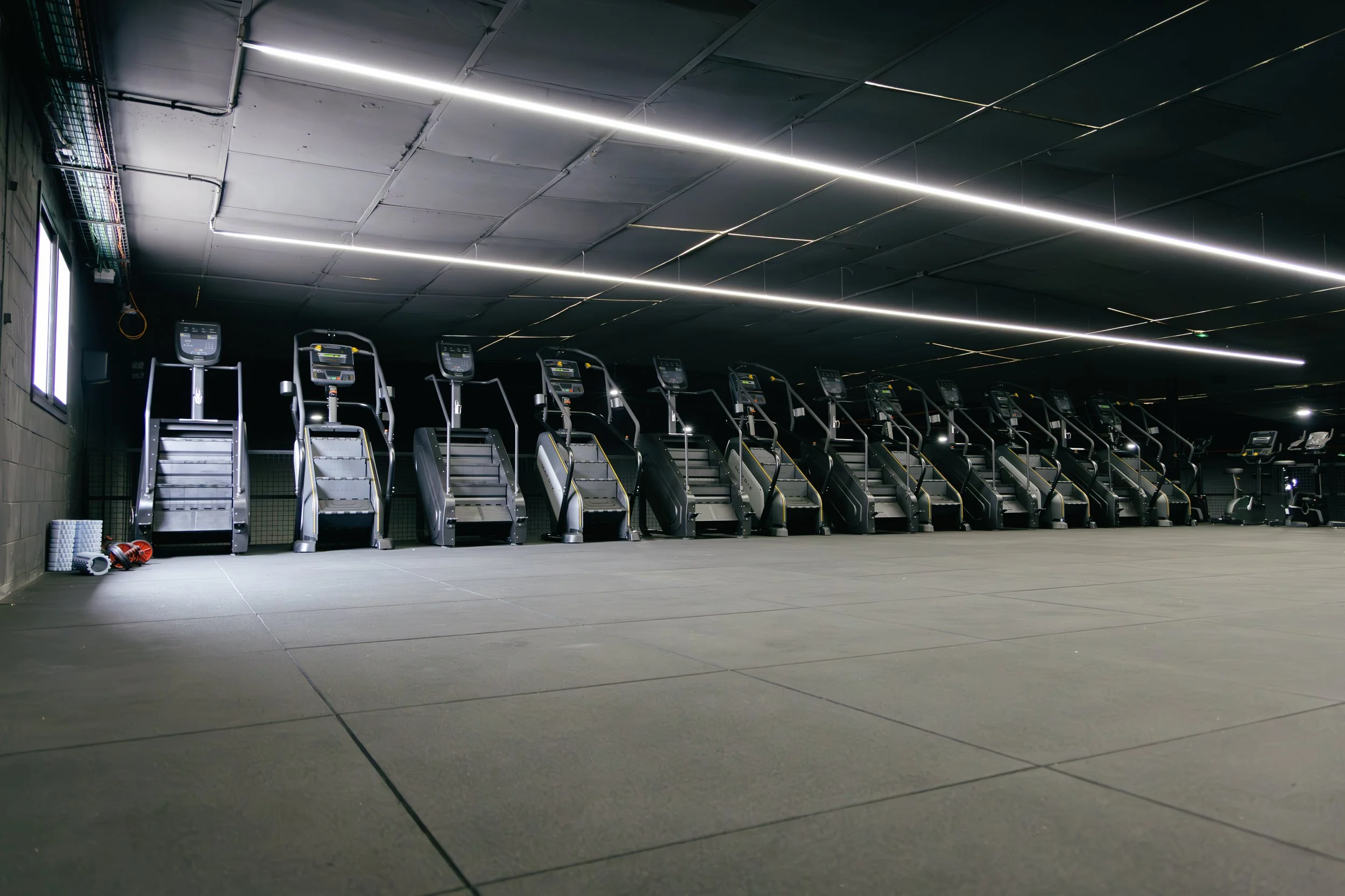Sala de entrenamiento vacía con varias máquinas de correr en un gimnasio moderno con luces LED en el techo.