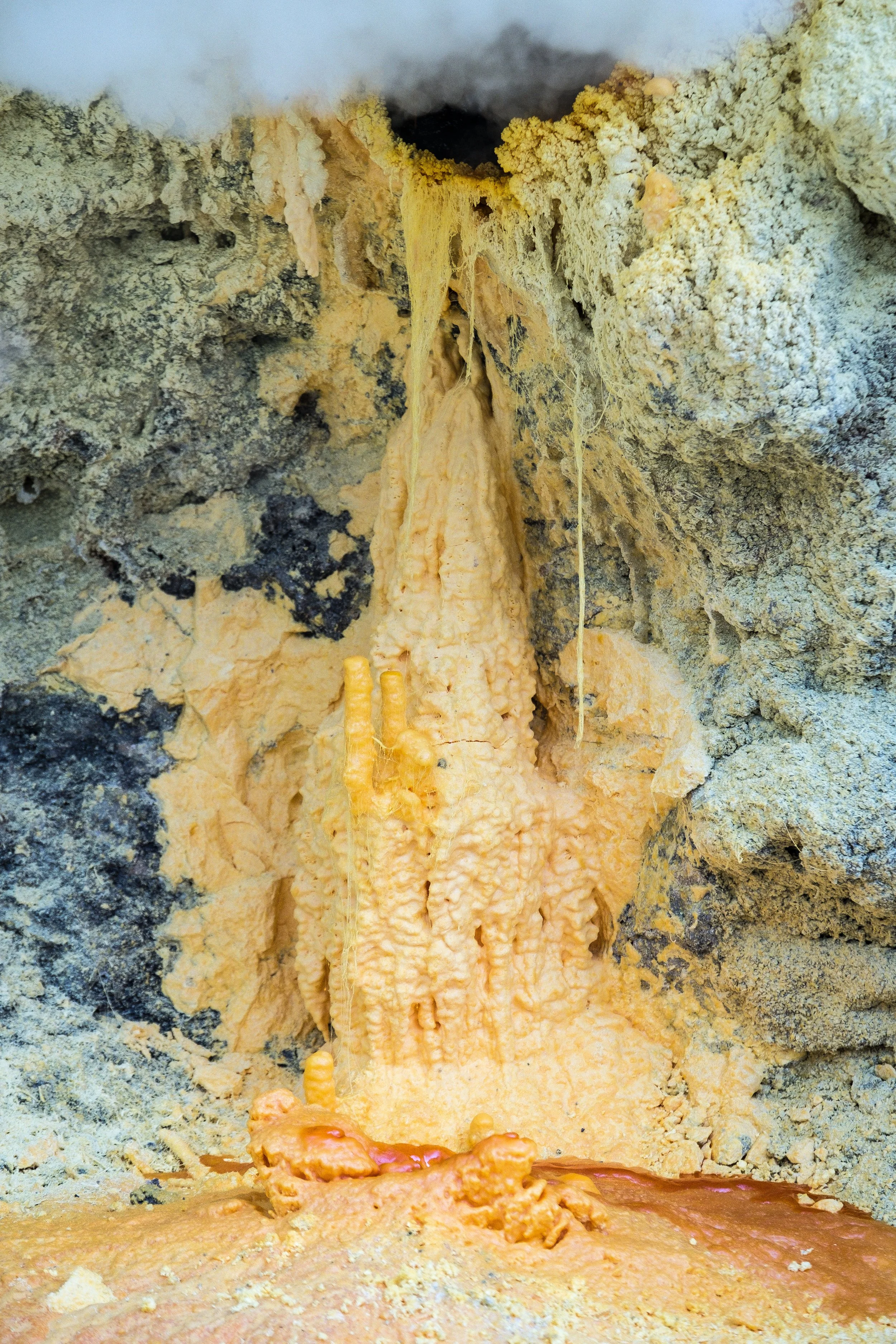 Une formation rocheuse avec des stalactites et des dépôts de minéraux orange, formant une sculpture de soufre.