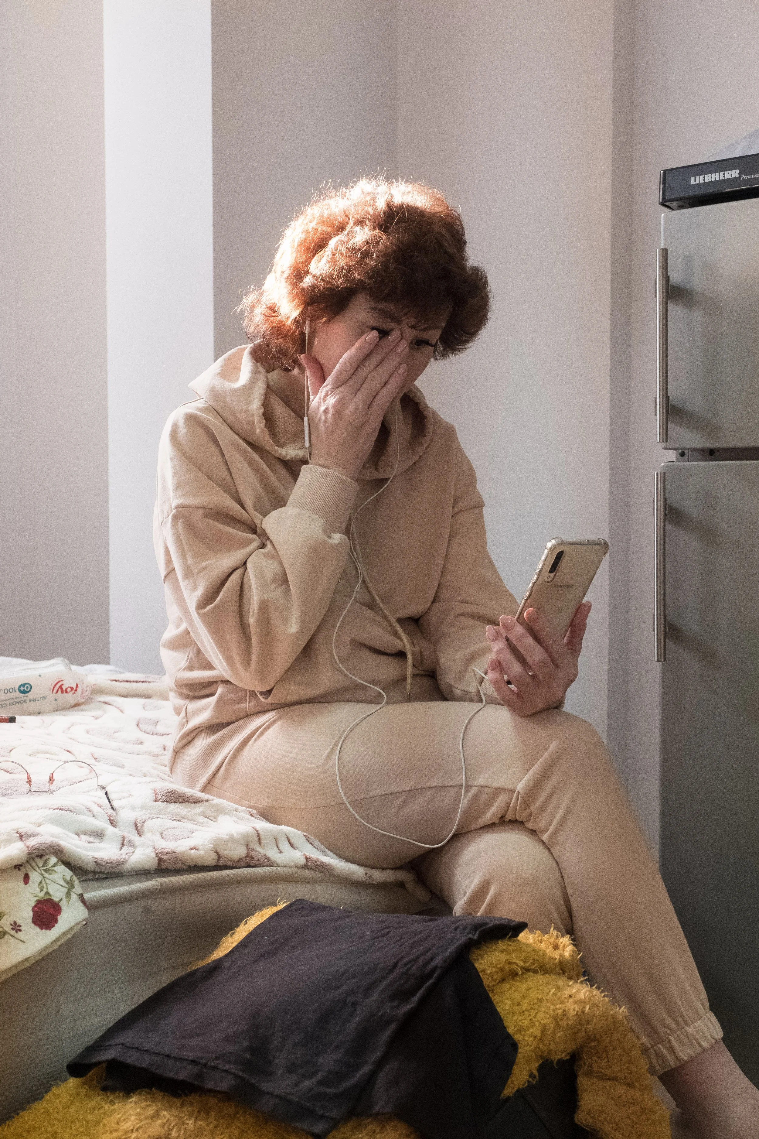 Une réfugiée ukrainienne assise sur un lit, en pleine conversation un téléphone portable à la main, verse quelques larmes.