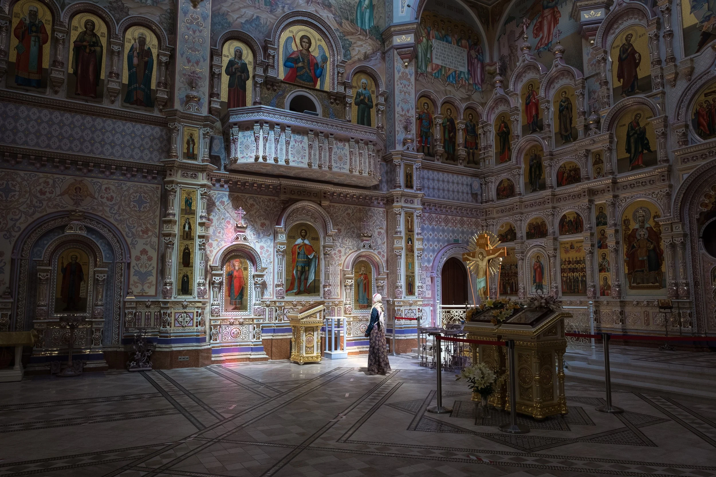 Intérieur d'une église orthodoxe ornée de nombreuses icônes et fresques religieuses, avec une femme priant près du crucifix en Biélorussie.