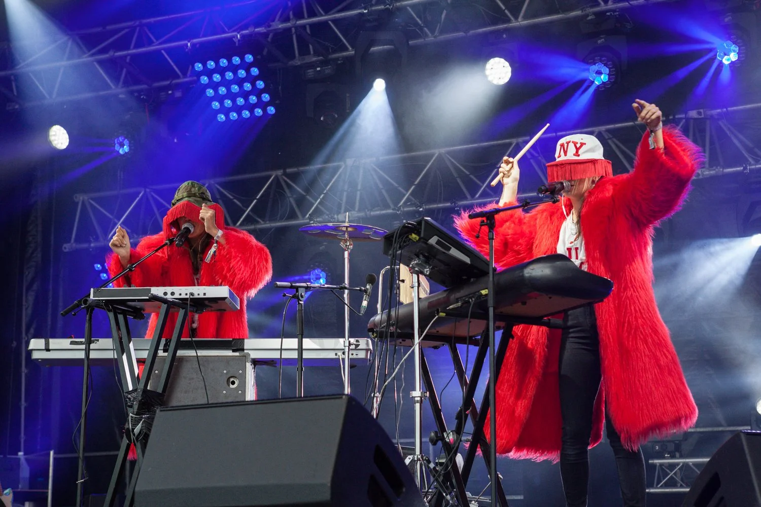 Deux musiciens en costume rouge avec des couvre-chefs jouant lors d'un concert sur scène, sous des lumières colorées.