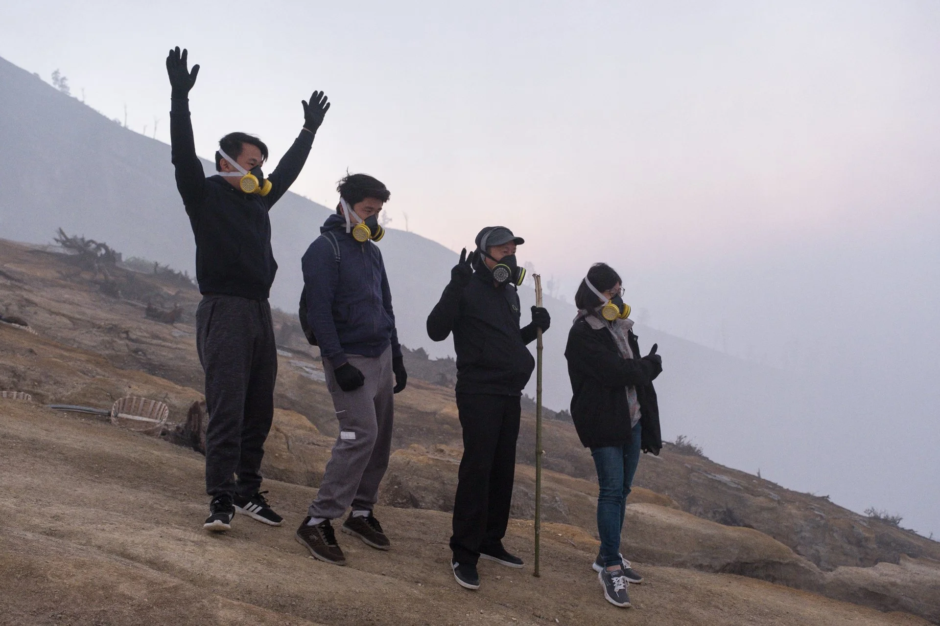 Cinq personnes portant des masques à gaz et des vêtements chauds, debout sur un terrain rocheux, posent pour une photo au Kawah Ijen lors d'une journée où les gaz toxiques emplissent l'air.