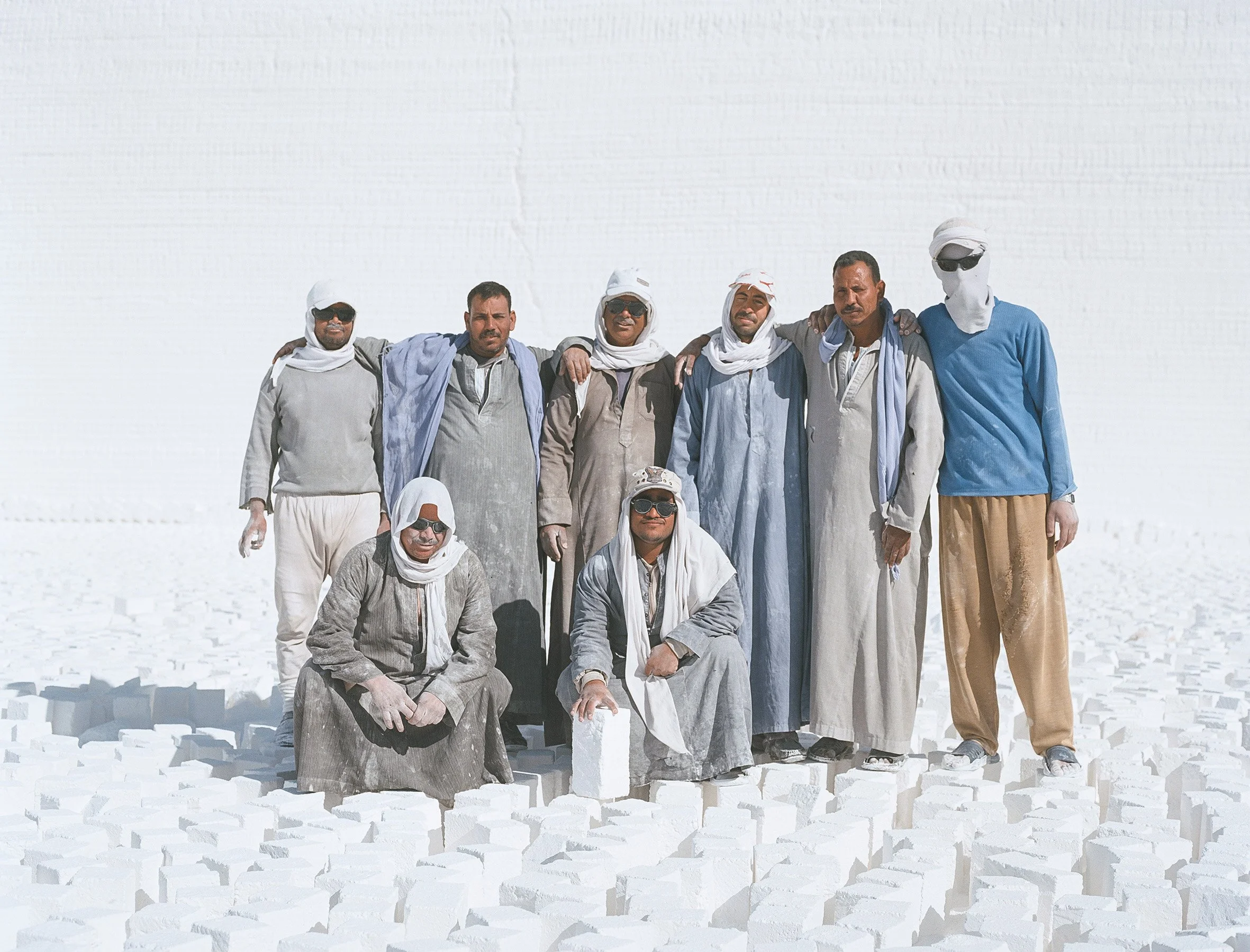 Groupe de neuf hommes dans une carrière de calcaire, certains portant des vêtements traditionnels et des foulards pour se protéger du soleil, posant pour une photo.