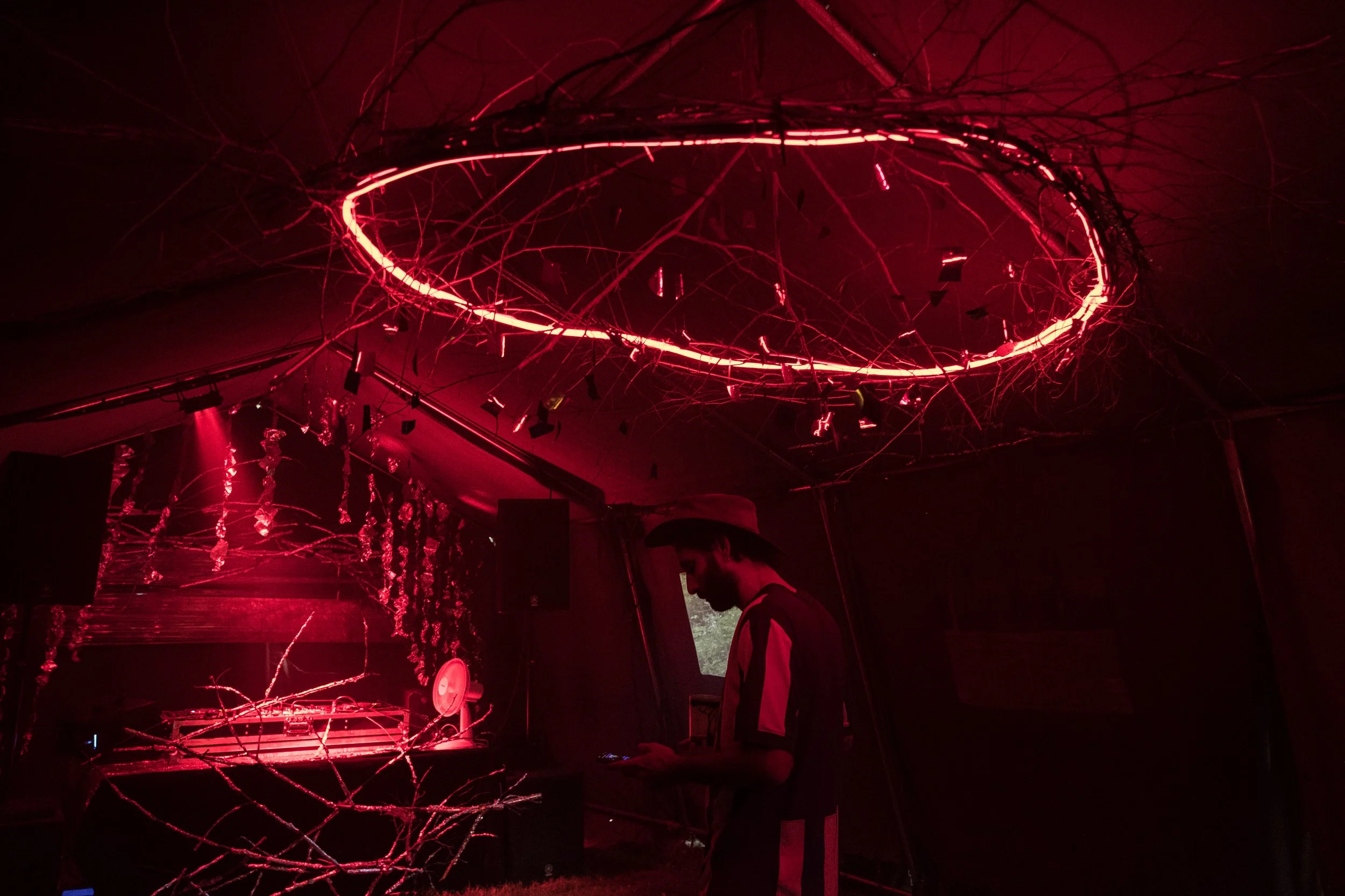 Une personne debout dans une pièce sombre éclairée par des néons rouges, avec un plafond orné de cercles lumineux et de branches décoratives.