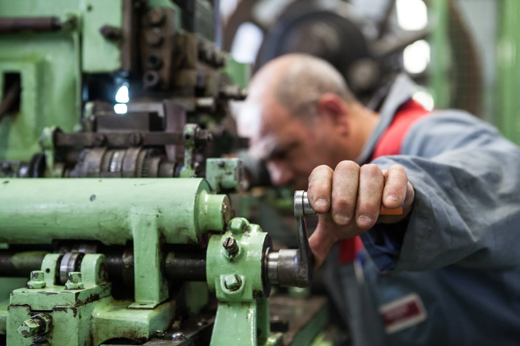 Un homme travaille sur une machine industrielle, appuyé contre l’équipement avec sa main gauche, dans un atelier