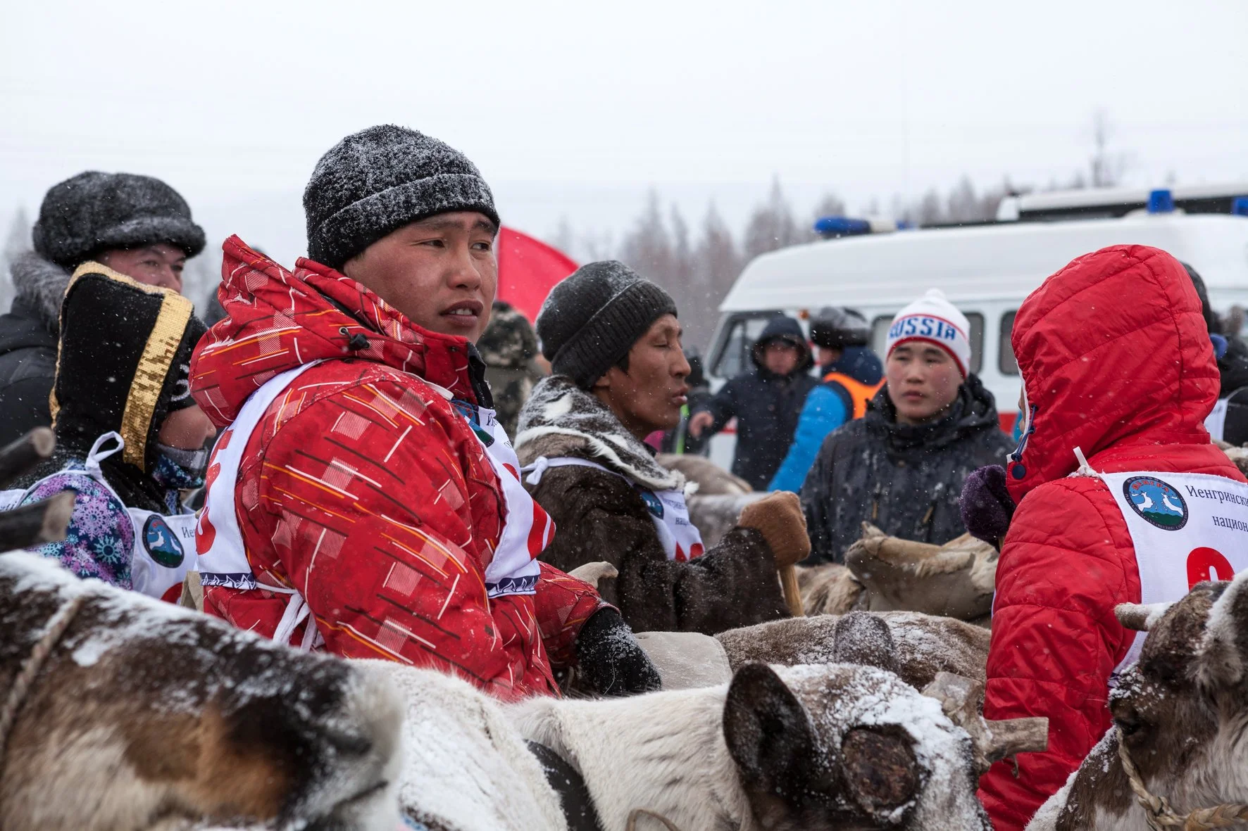 Groupe de personnes vêtues de vêtements chauds, avec des rennes, en milieu enneigé, lors d'un rassemblement outdoor en hiver.