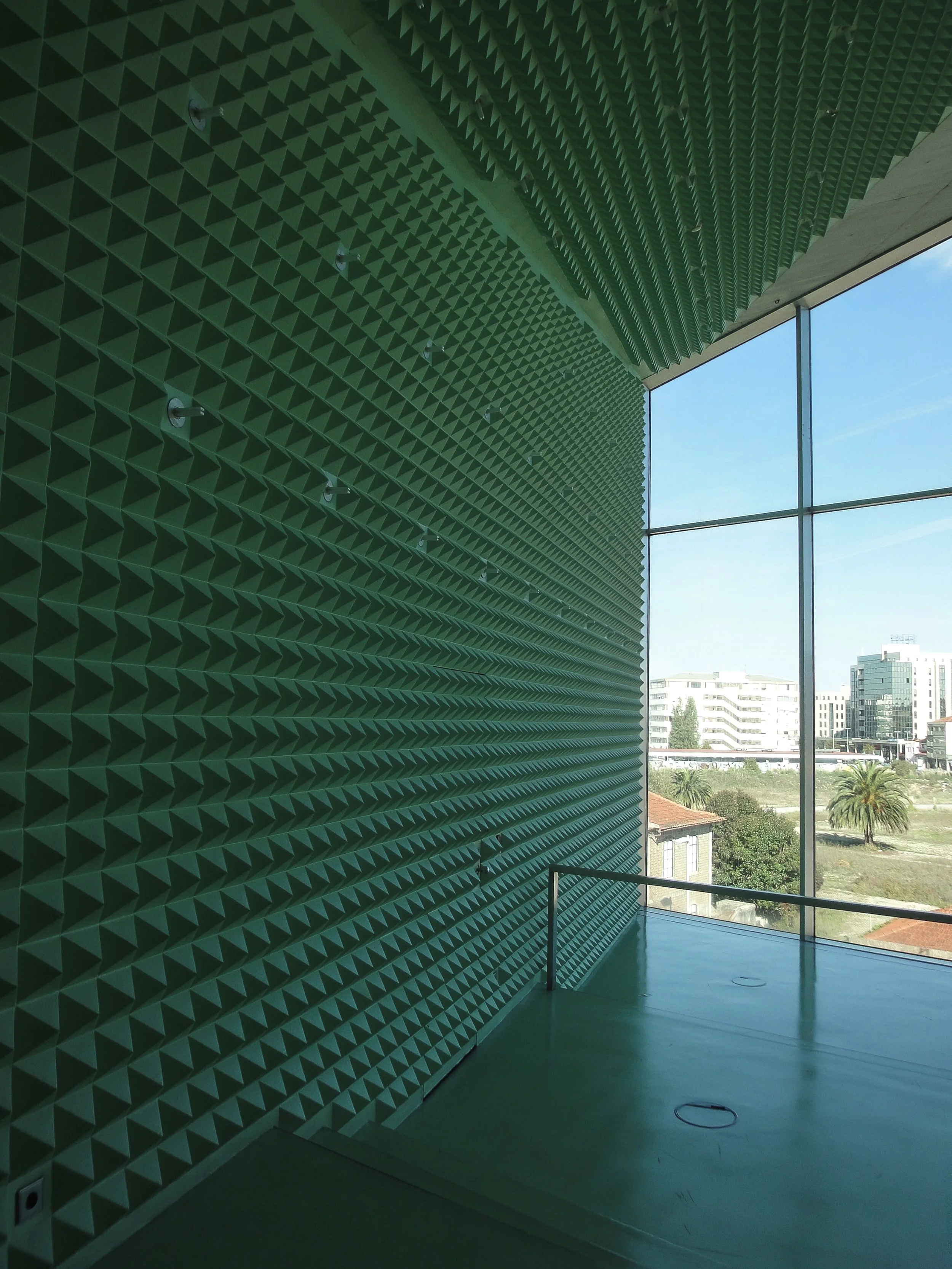 Intérieur de la casa de musica à Porto avec un mur en mousse acoustique vert et un grande paroi de verre donnant sur une ville avec des bâtiments et des palmiers.
