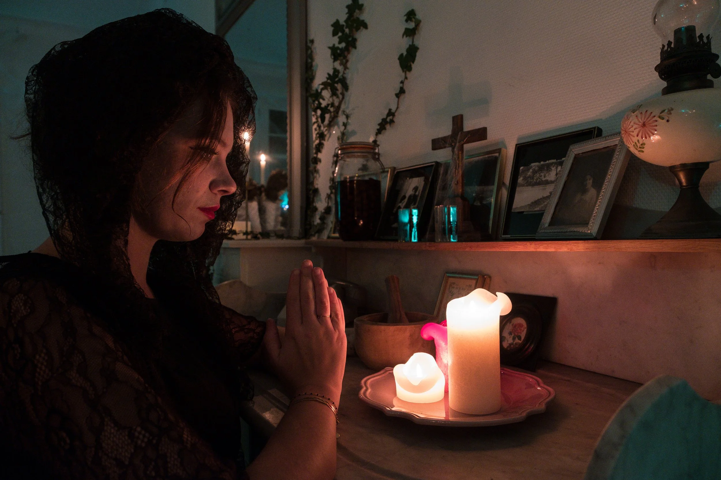 Une femme prie devant des bougies allumées dans une pièce sombre.