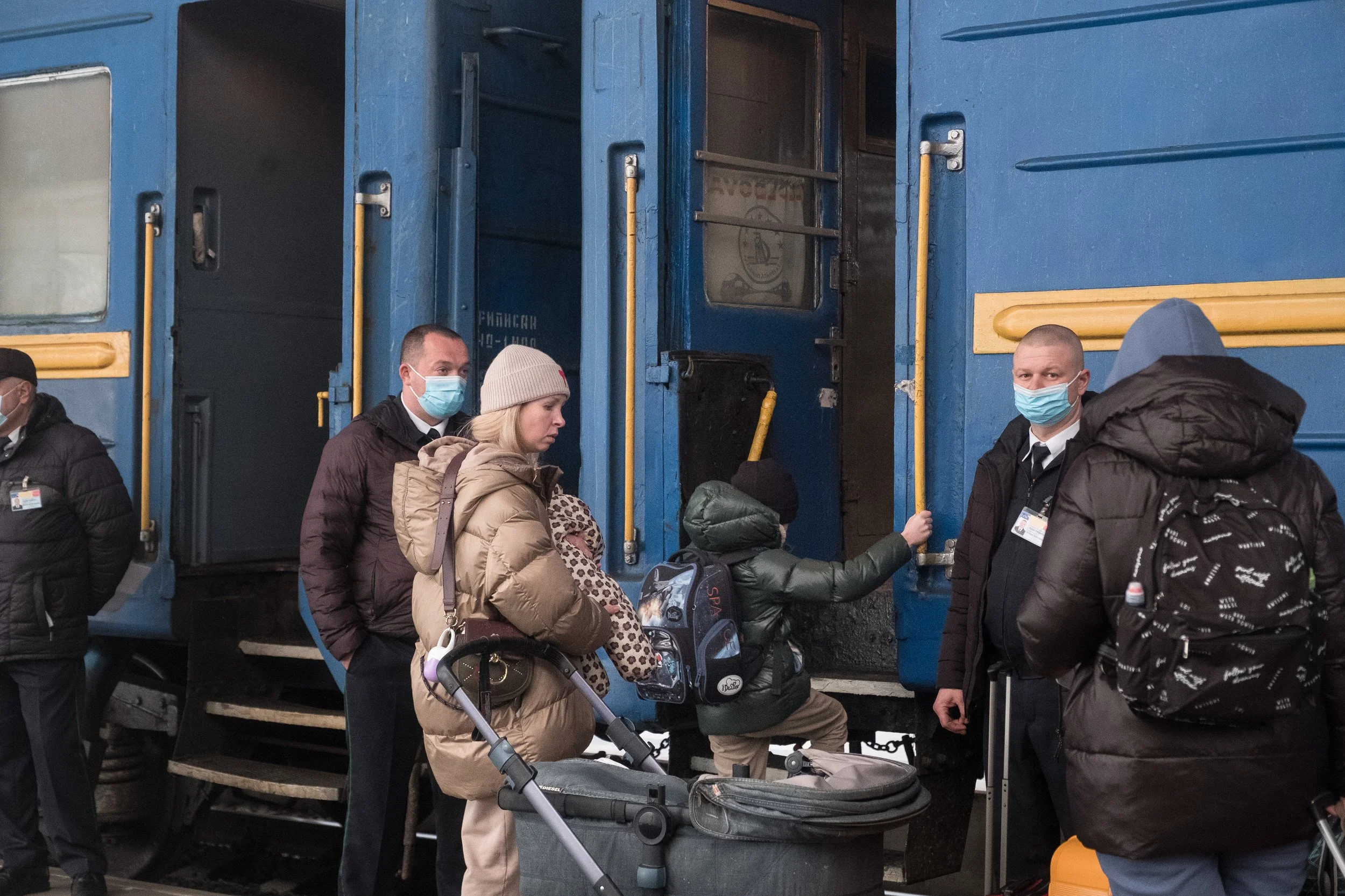Des réfugiés ukrainiens portant des masques faciaux attendent de monter dans un train bleu, avec des valises et sacs à bagages, à la gare de Chisinau.
