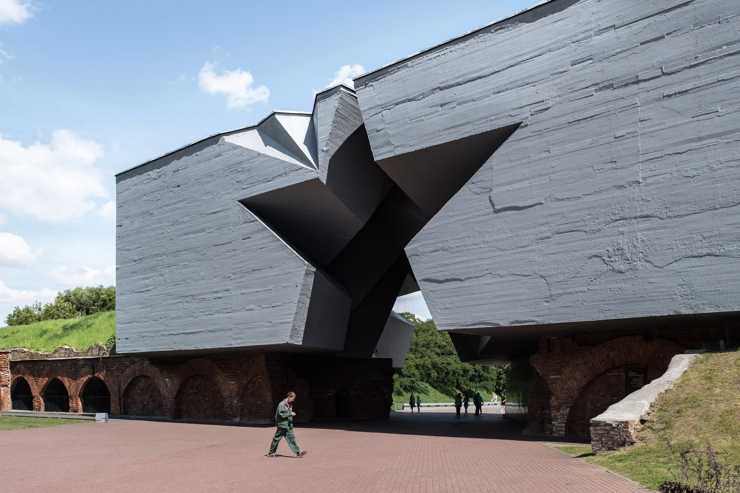 Bâtiment moderne en béton gris avec des formes géométriques angulaires, avec des personnes marchant en dessous dans une zone piétonne extérieure en Biélorussie.