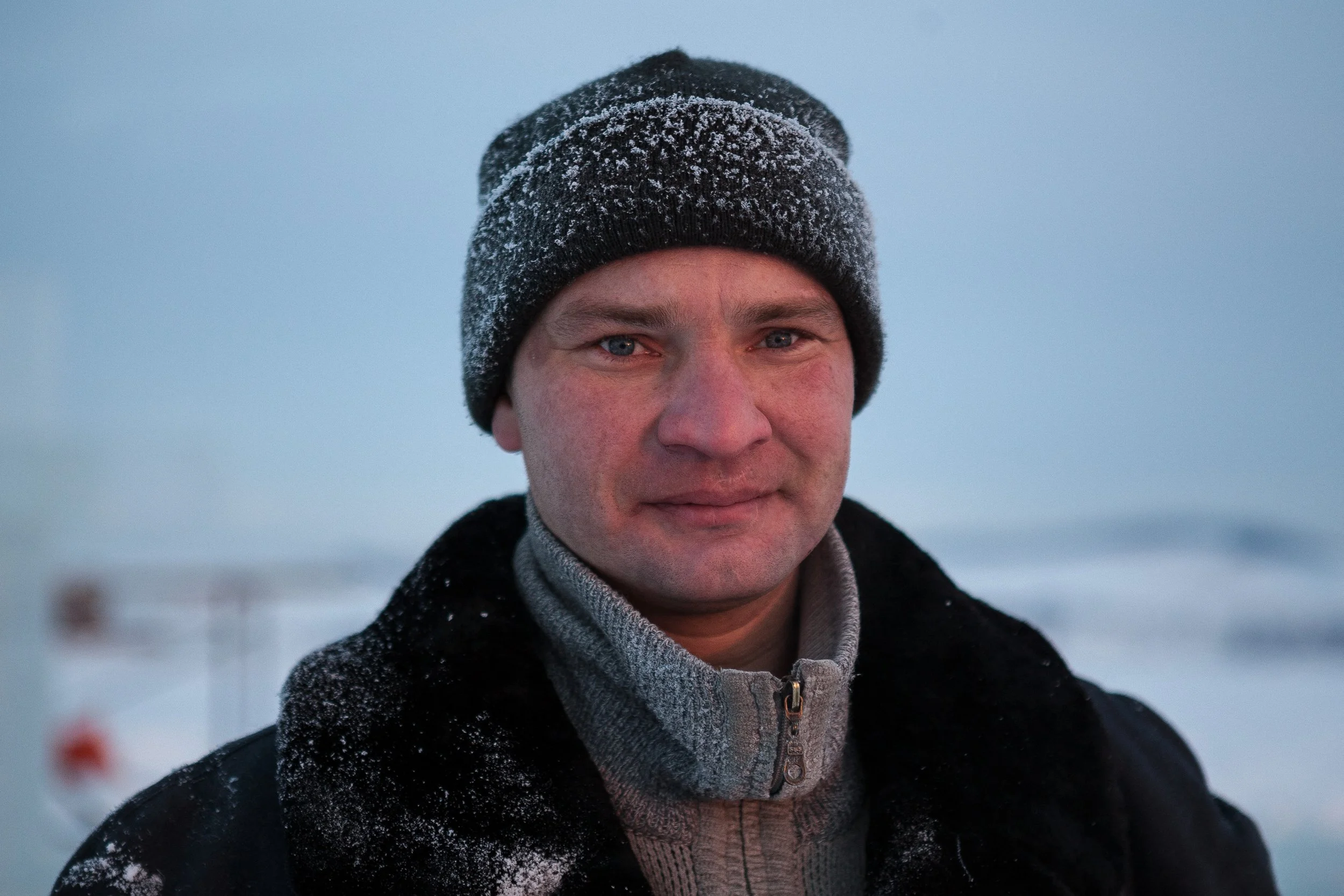 Un homme avec un bonnet gris, des traits froids, dans un paysage enneigé.
