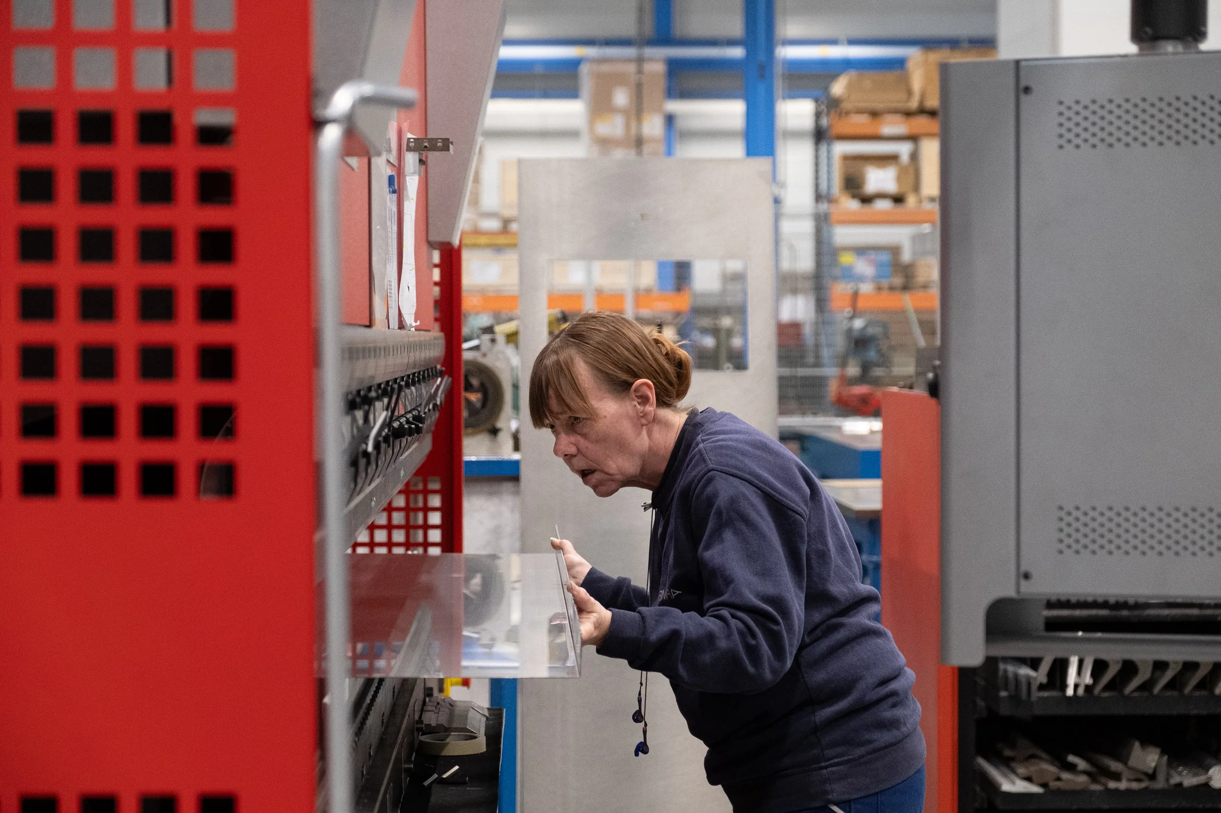 Une femme dans un entrepôt industriel, pliant des grandes plaques de tôle.