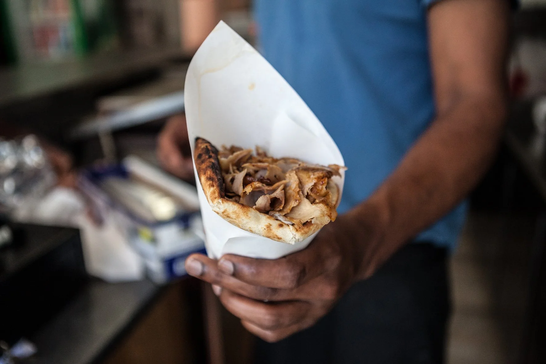 Une personne tient un kebab avec de la viande grillée dans une main, dans un établissement de restauration.