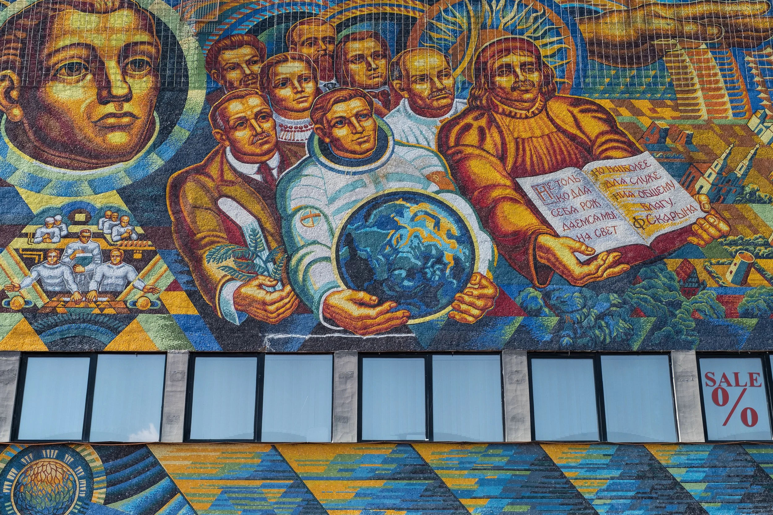 Une mosaïque soviétique murale colorée représentant des figures humaines avec des symboles soviets, y compris une représentation de la Terre, et une scène industrielle, évoquant le socialisme ou le communisme russe.