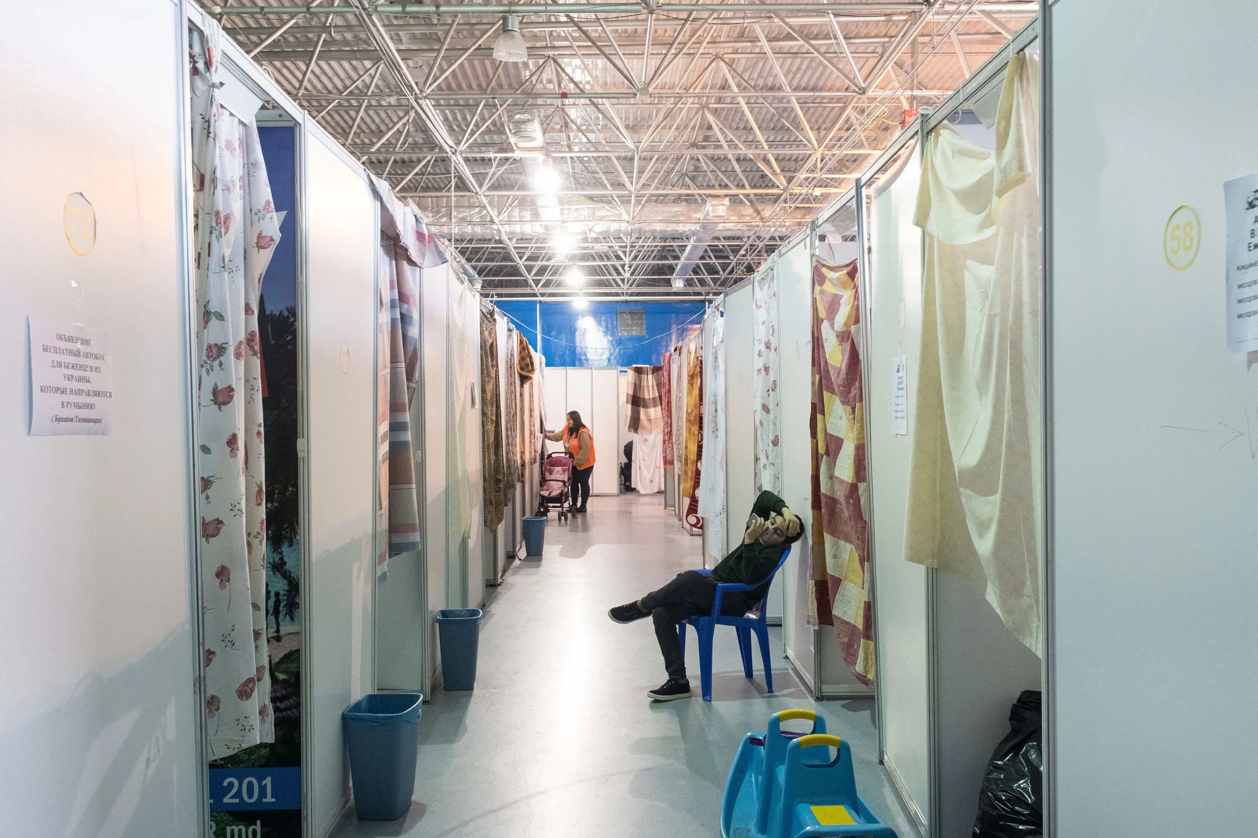 Une rangée de chambres temporaires dans un gymnase avec des rideaux, quelques personnes, dont une assise sur une chaise en Moldavie.