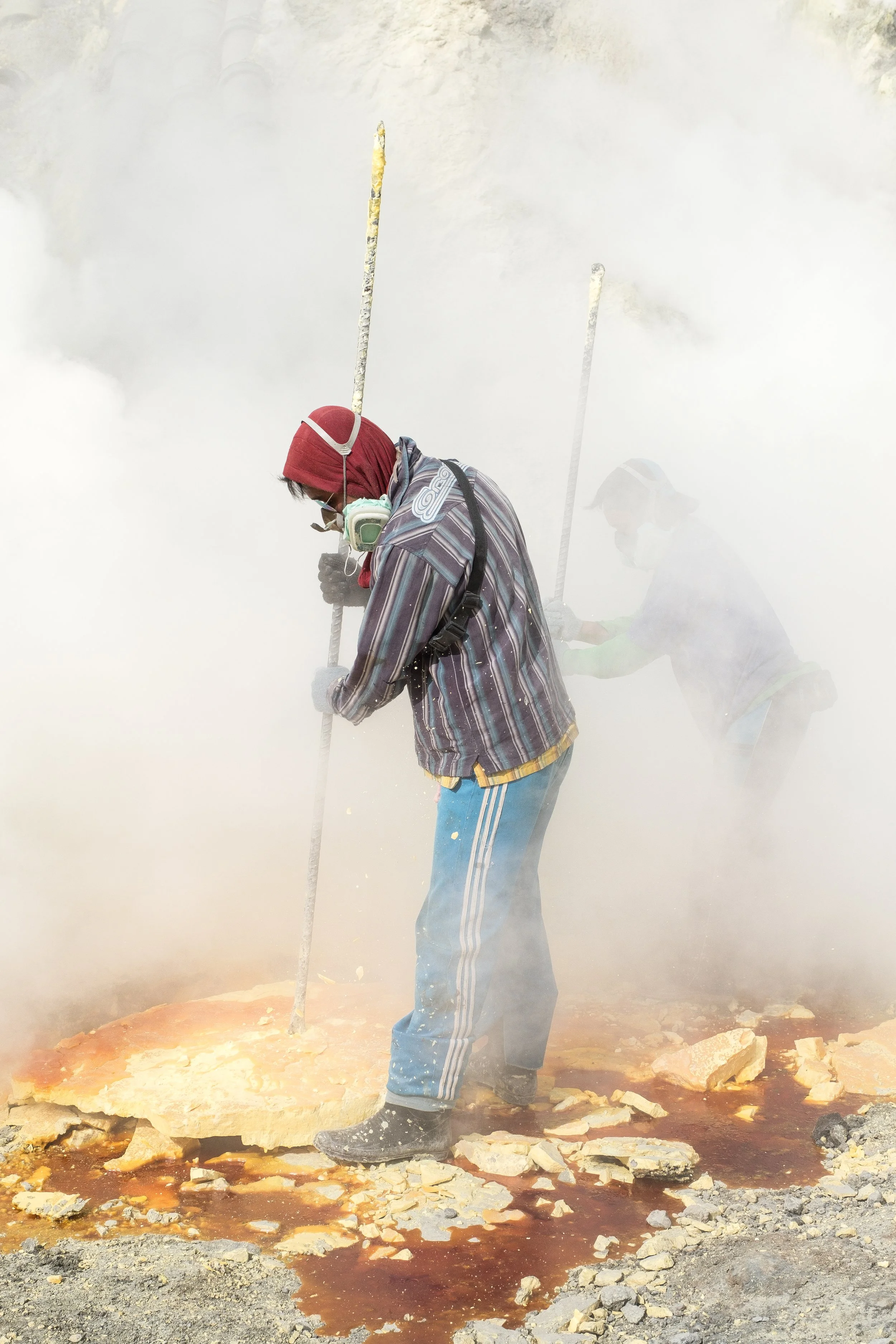 Deux personnes entourées de gaz toxique, brisant des morceaux de soufre. Ils portent des vêtements de protection.