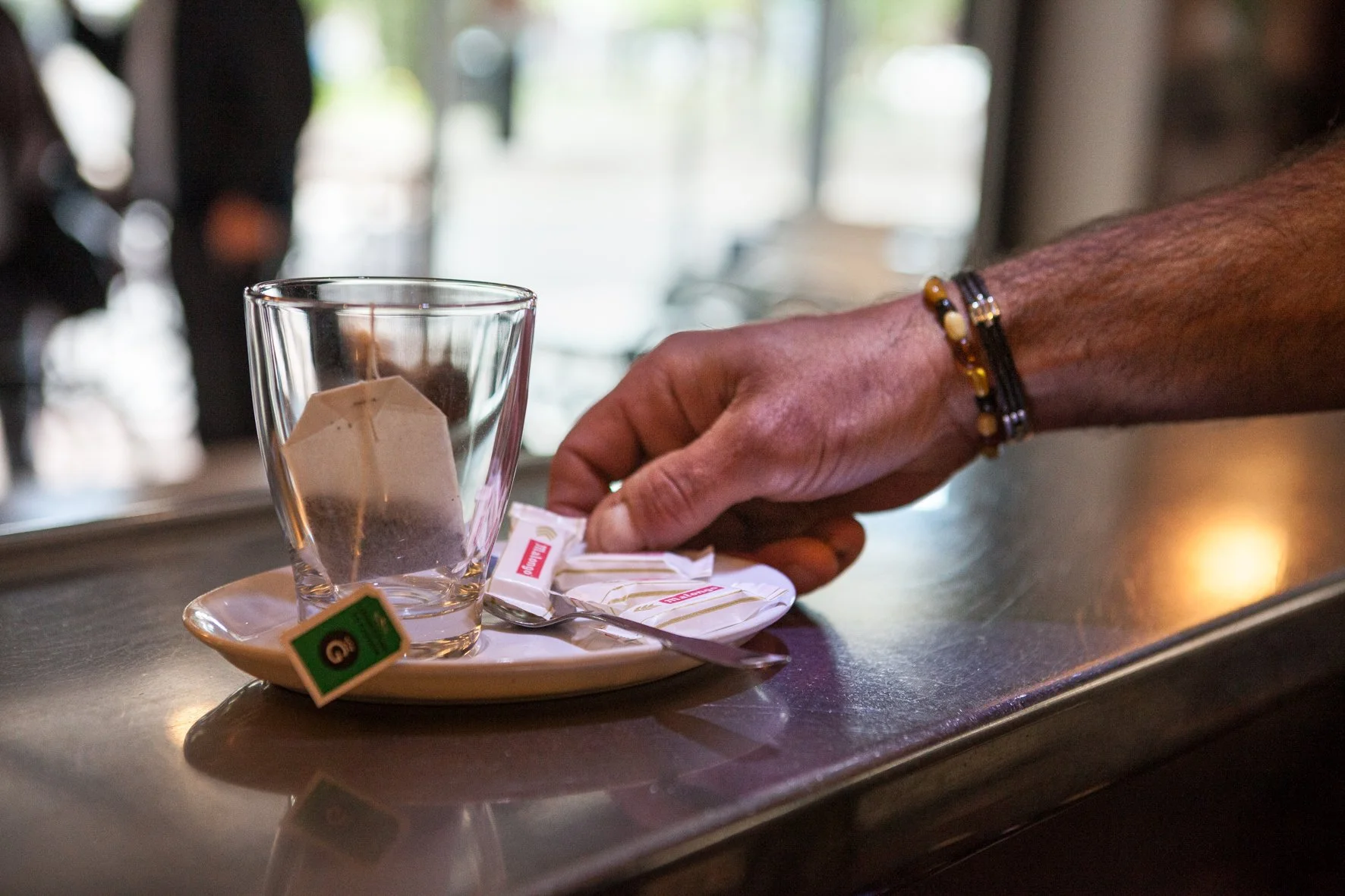 Main tenant une tasse avec un sachet de thé, des sachets de sucre et une cuillère sur une petite soucoupe dans un café ou un restaurant.