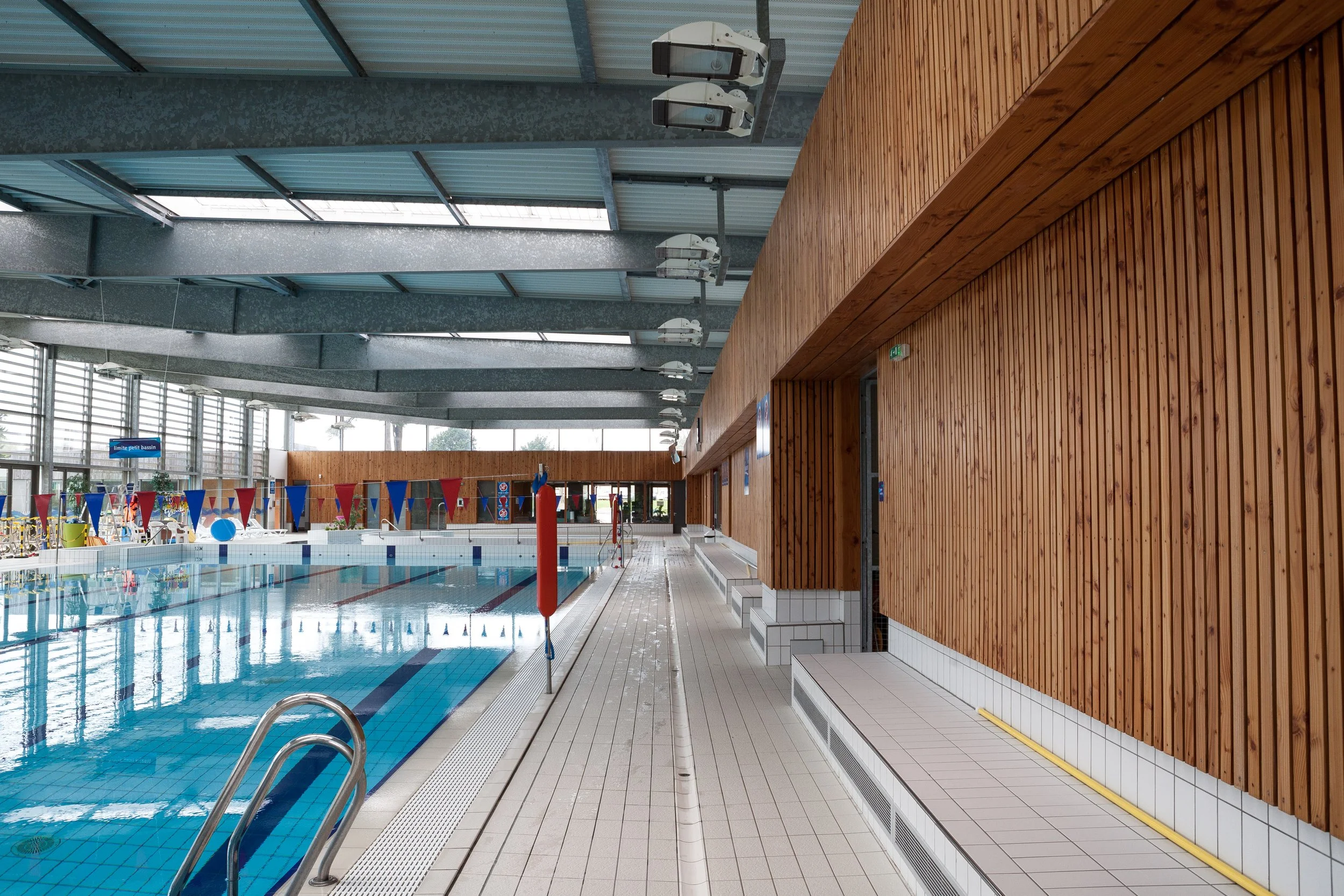 Piscine intérieure avec lignes de natation, décor en bois, et espaces de repos le long du mur.