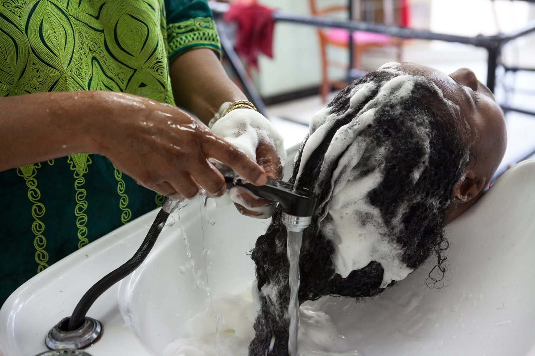 Une personne reçoit un shampoing dans un salon de coiffure, la tête dans un lavabo, de l'eau et du shampoing mousseux sur ses cheveux.