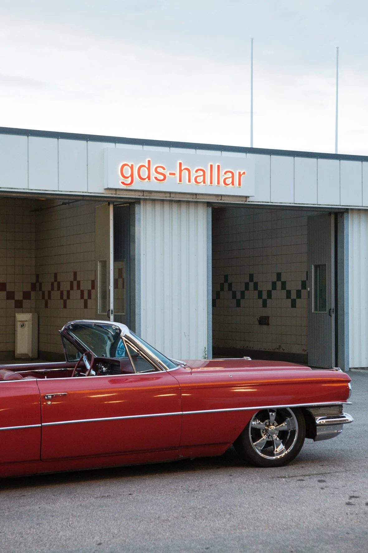 Voiture classique rouge garée devant un bâtiment avec le panneau 'gds-hallar'.