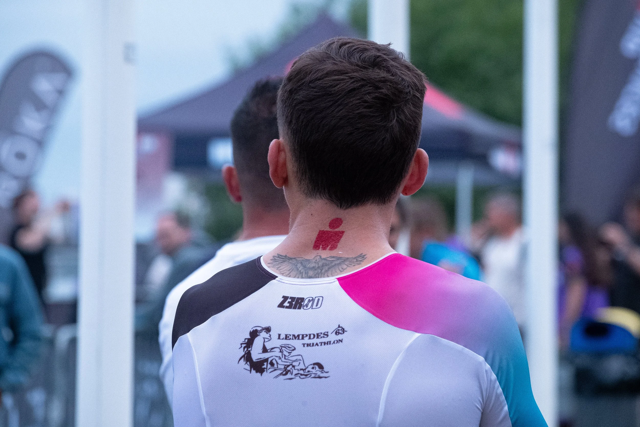 Jeune homme vu de dos portant un maillot de triathlon avec le logo 'Lempdes Triathlon 63' et un tatouage dans le cou, lors d'un Ironman en plein air à Tours.
