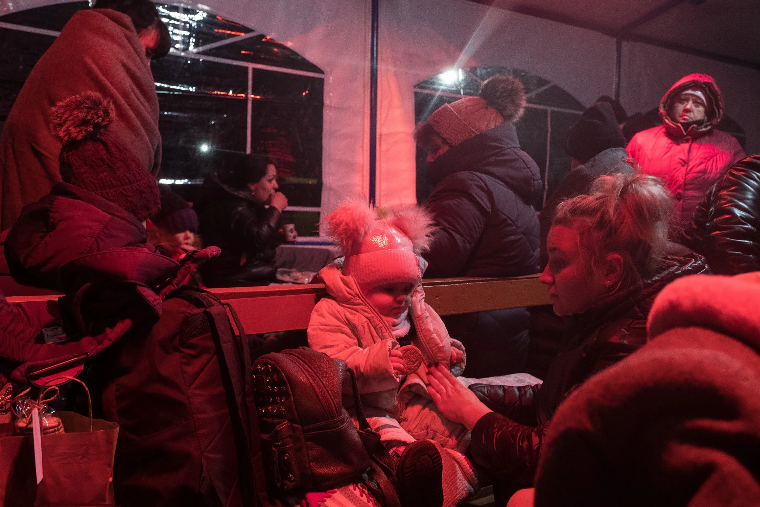 Groupe de réfugiés ukrainiens en vêtements d'hiver à l'intérieur d'une tente, certaines assises sur des bancs, discutant et prenant des boissons, ambiance hivernale.