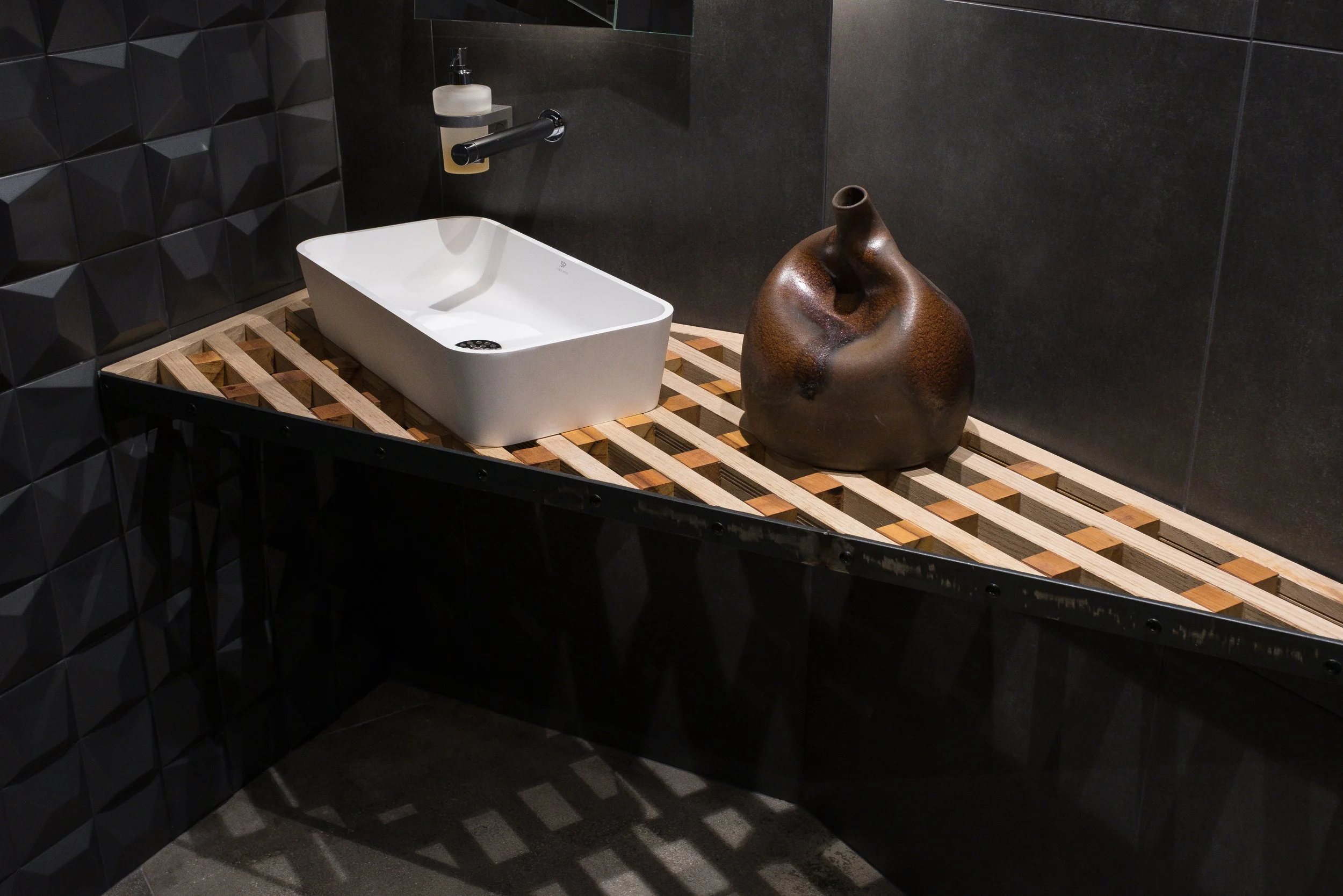Vasque blanche rectangulaire et décoration en pot en céramique brun, dans une salle de bain moderne avec murs en carrelage noir