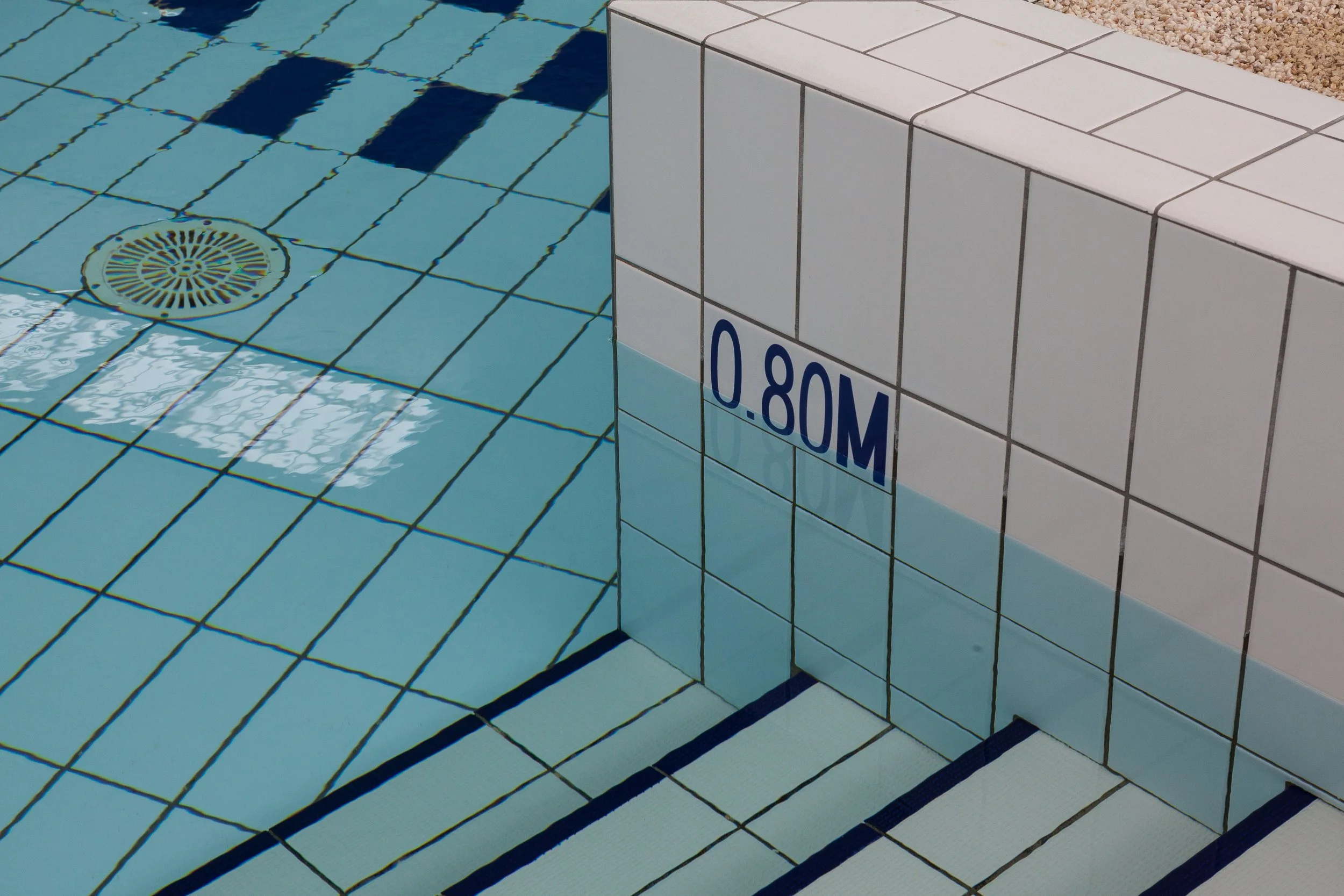 Plancher de piscine avec marquage de profondeur 0.80 m, délimités par des carreaux blancs et bleus, avec drain d'évacuation.