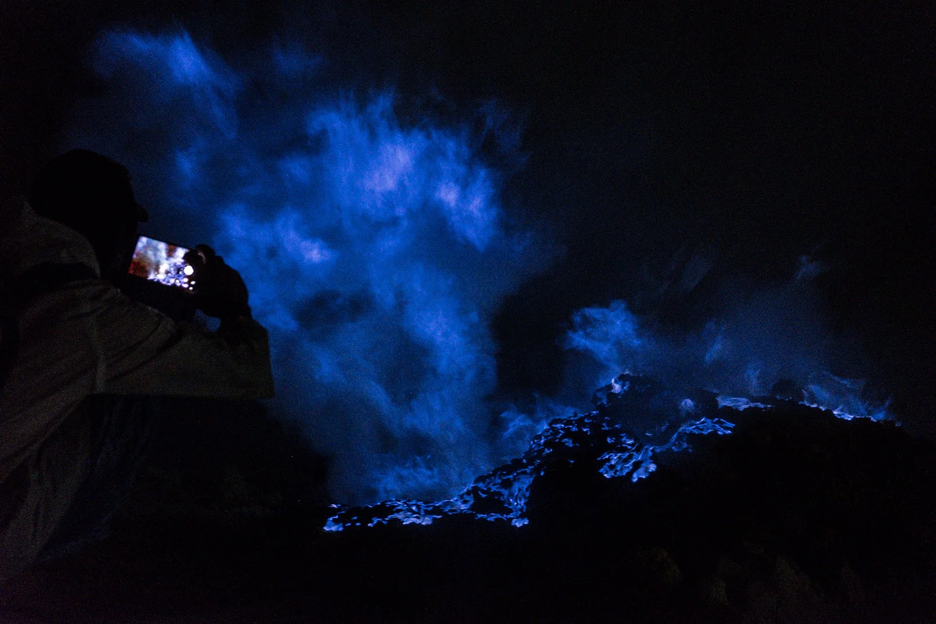 Une personne en train de prendre une photo ou vidéo de flammes bleues dans la nuit au Kawah Ijen, en Indonésie.