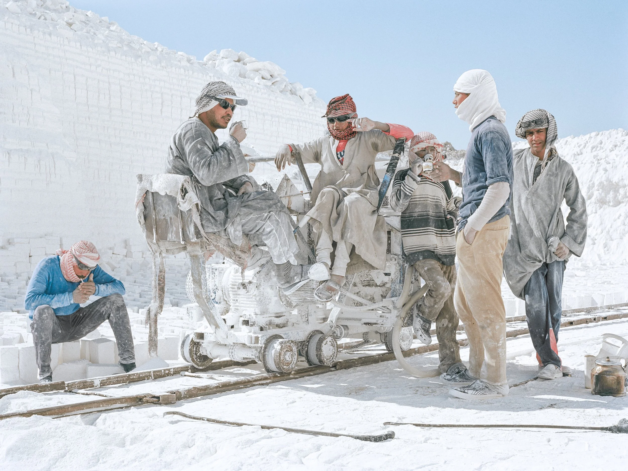 Groupe de personnes dans une carrière de calcaire, certaines assises sur une énorme scie circulaire, portant des vêtements protecteurs, devant une grande paroi de calcaire.