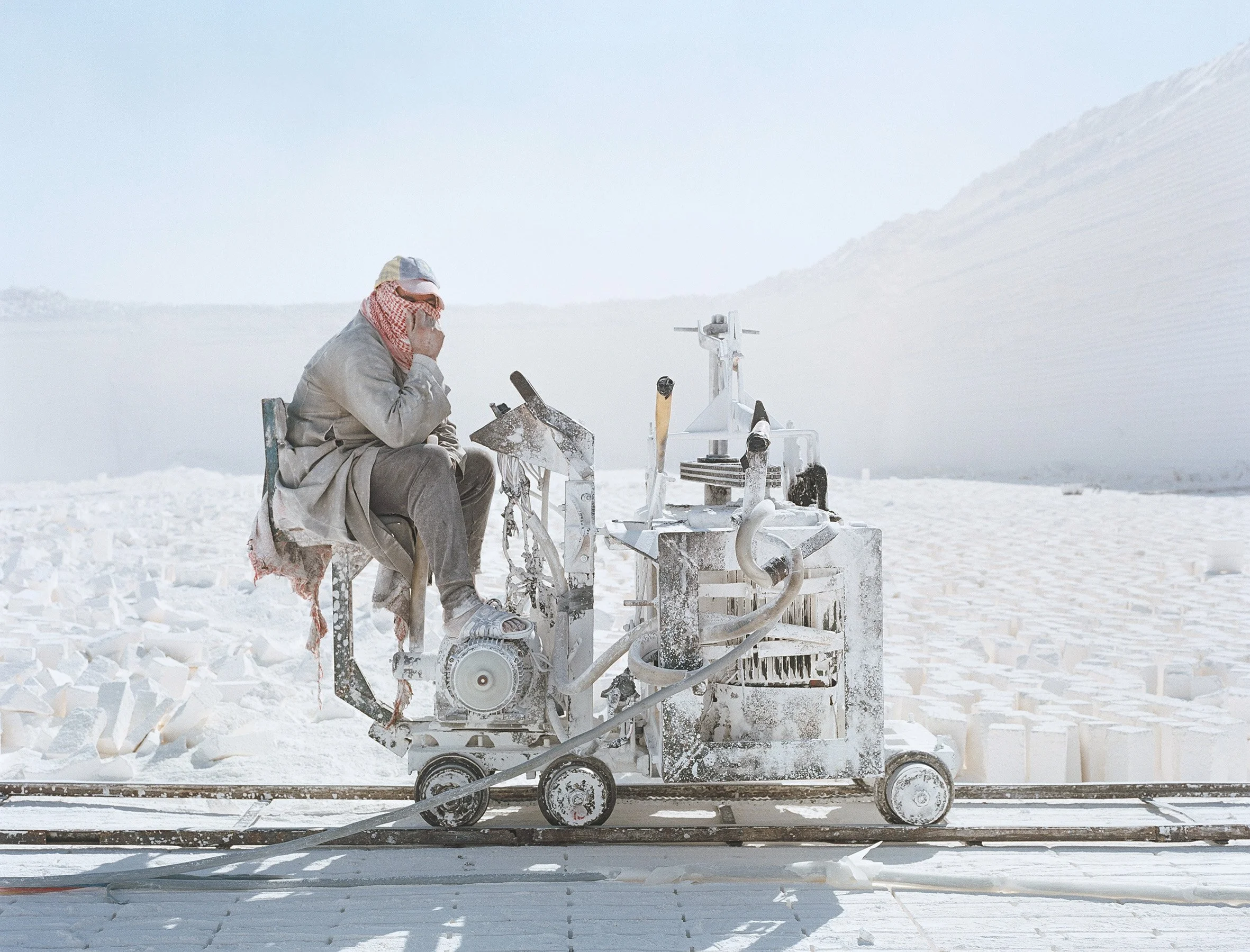 Un homme assis sur une machine en plein désert blanc, portant un foulard rouge et blanc sur le visage.