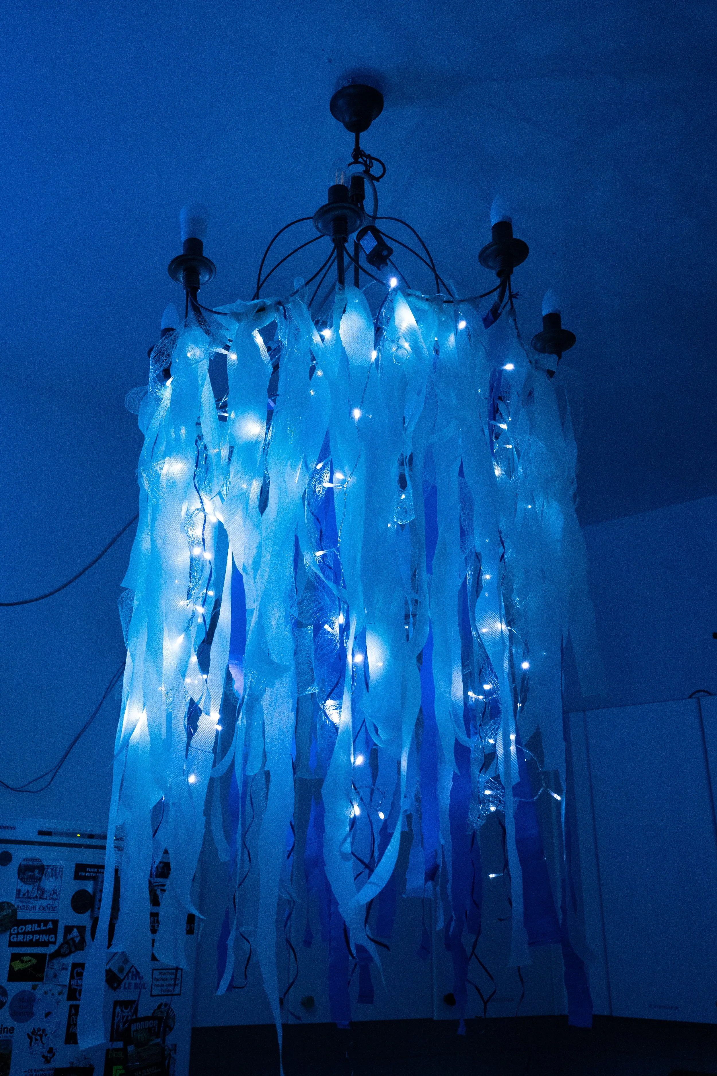 Un lustre décoré avec des rubans blancs et des lumières LED bleues, suspendu au plafond.