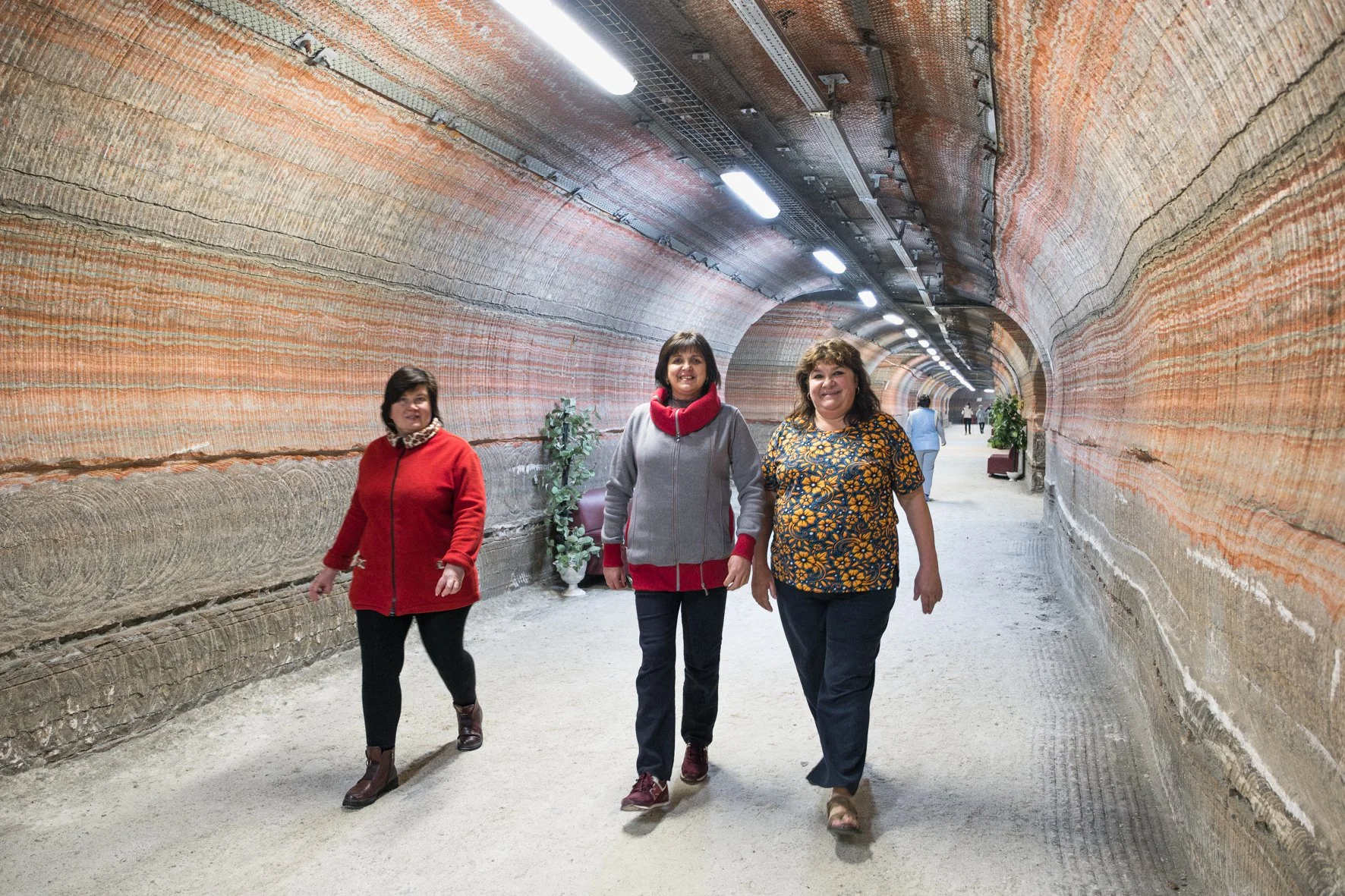 Trois femmes marchant dans un tunnel avec des murs en roche stratifiée, éclairé par des lumières LED à Soligorsk, en Biélorussie.
