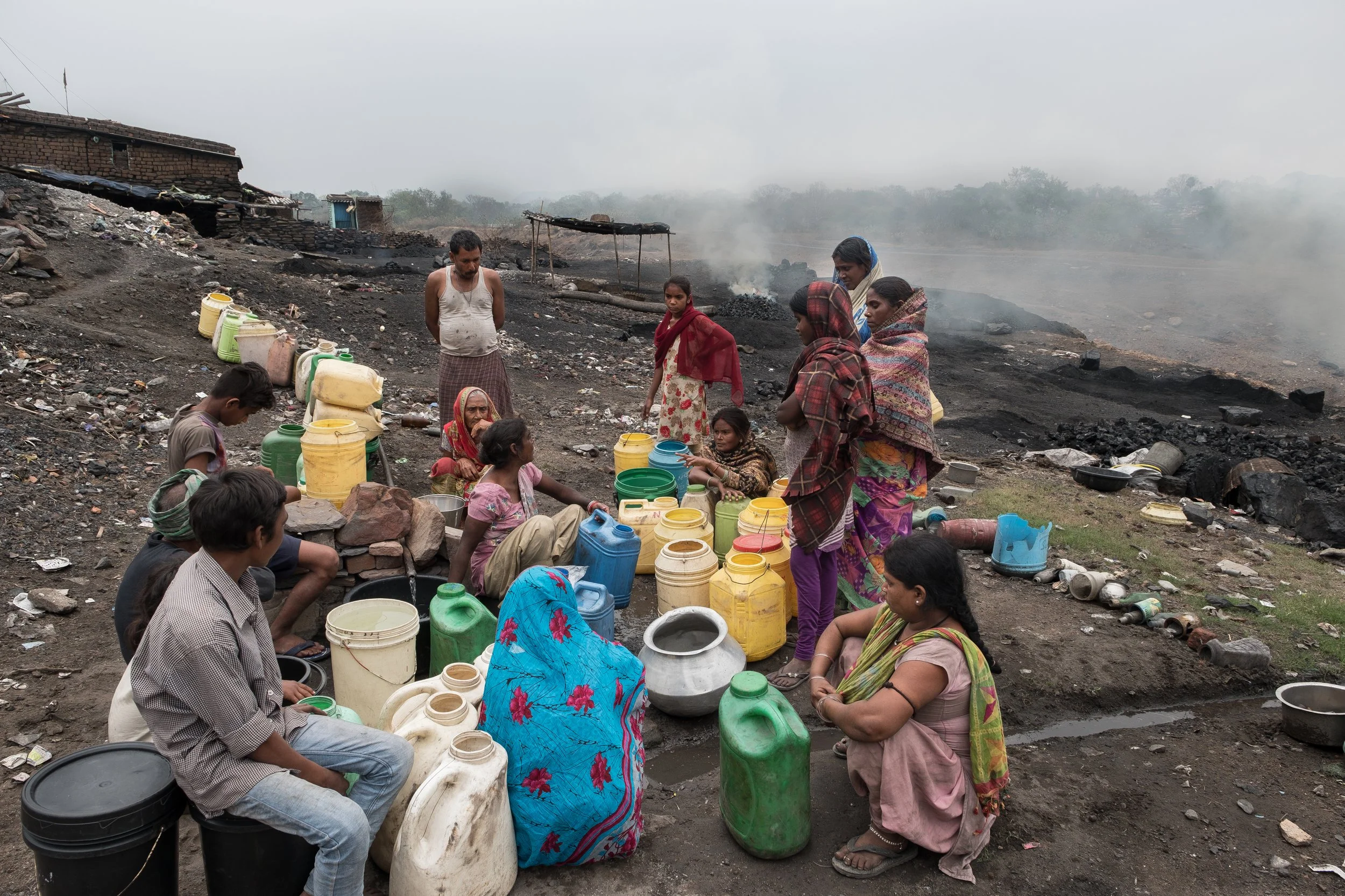 Groupe de personnes en Inde recueillant de l'eau dans un environnement aride et dénué de plantes avec des ruines et de la fumée en arrière-plan.